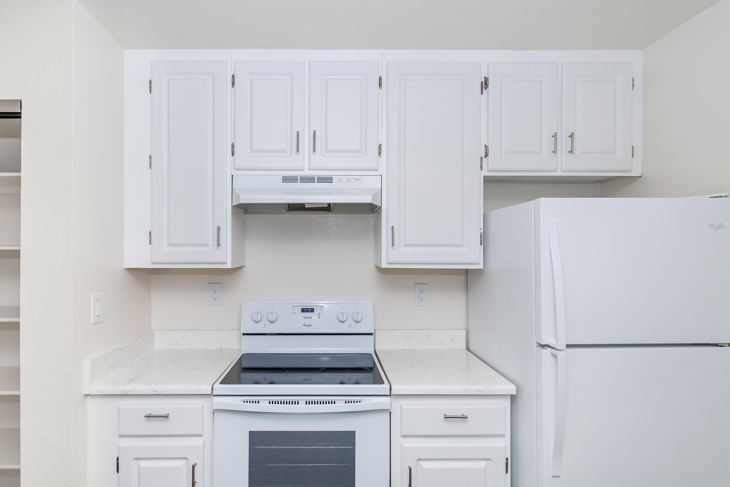 Modern kitchen with white cabinetry, a stainless steel stove, a microwave above it, and a white refrigerator. The countertops are light-colored, and the walls are painted a neutral color, creating a clean and bright atmosphere.