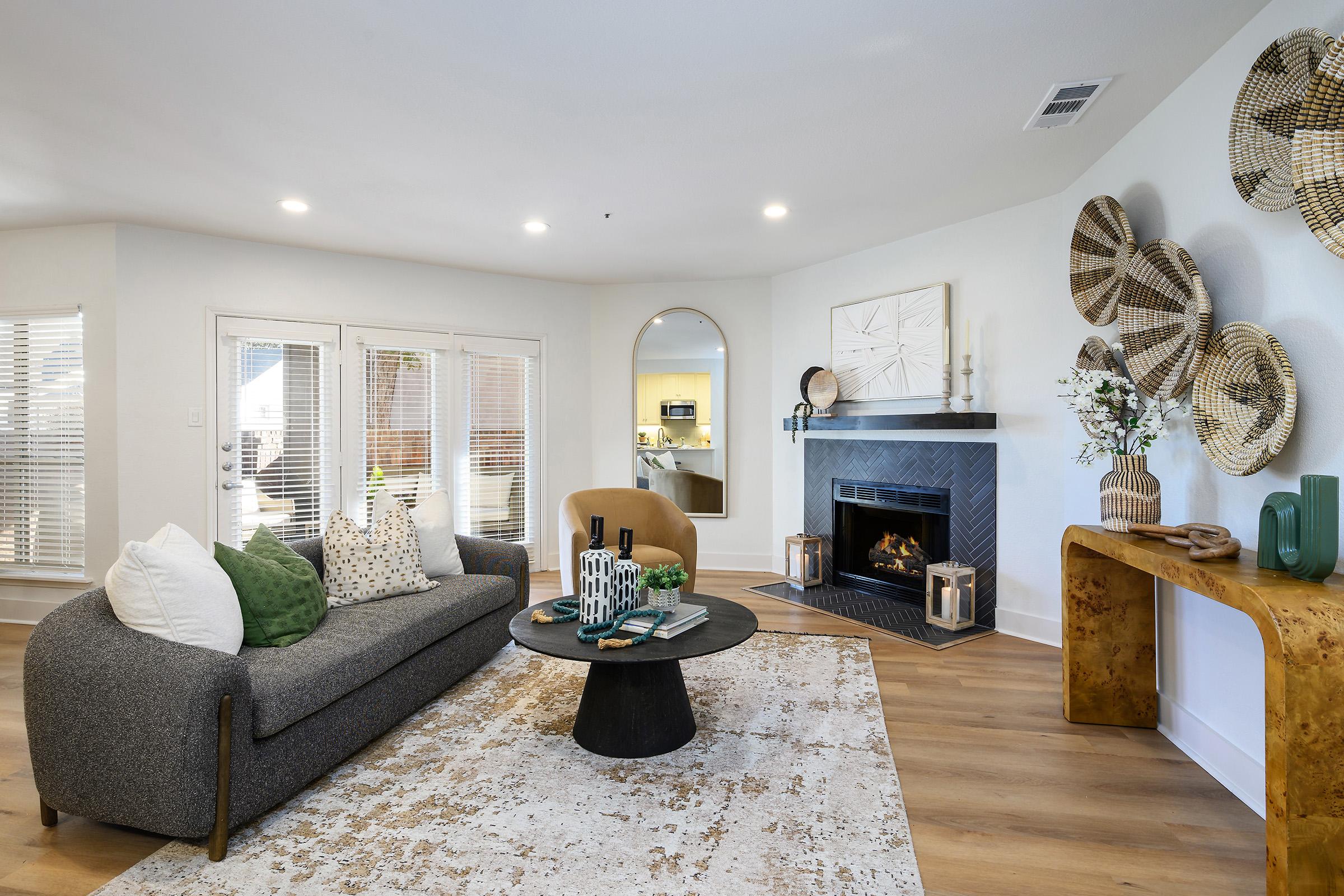 A modern living room featuring a cozy sofa with decorative pillows, a round coffee table, and a stylish fireplace. Natural light filters through large windows, and a decorative console table adds charm. Wall art and woven baskets enhance the decor, creating a warm and inviting atmosphere.