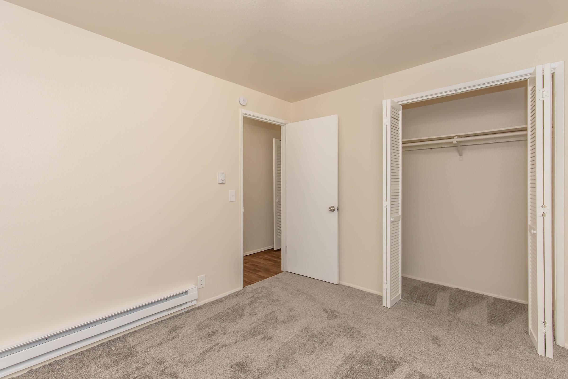 Empty room featuring light-colored walls, a carpeted floor, and a closet with sliding doors. A white door leads to another space, and there are no furnishings visible, creating an open and neutral atmosphere.