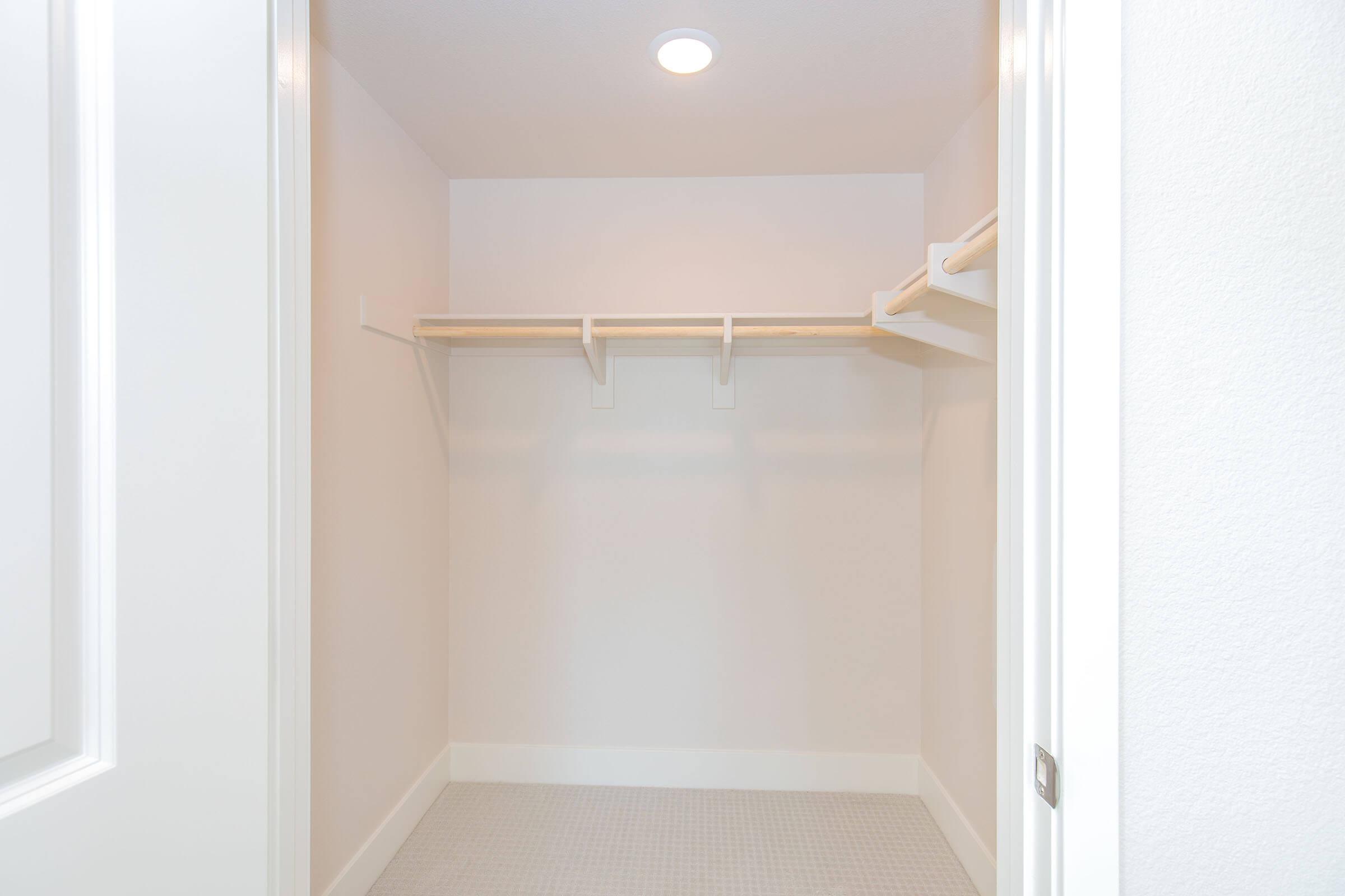 Empty walk-in closet with light-colored walls, featuring a ceiling light and two wooden shelves for storage. The closet has a clean and modern design, with ample space on the floor and a tiled surface.