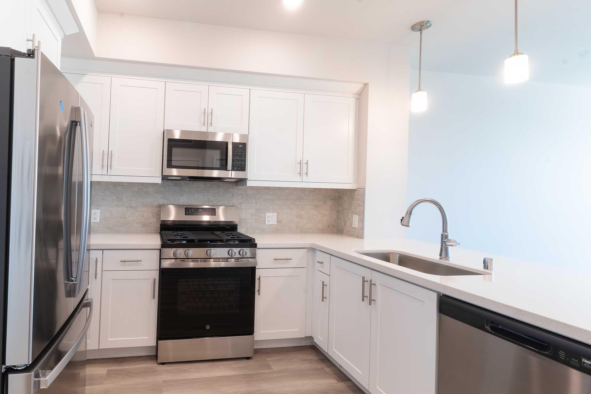 Modern kitchen featuring stainless steel appliances, including a gas range and microwave, white cabinets, and a sleek countertop. The space is well-lit with pendant lights and has a contemporary design, showcasing a blend of functionality and style.