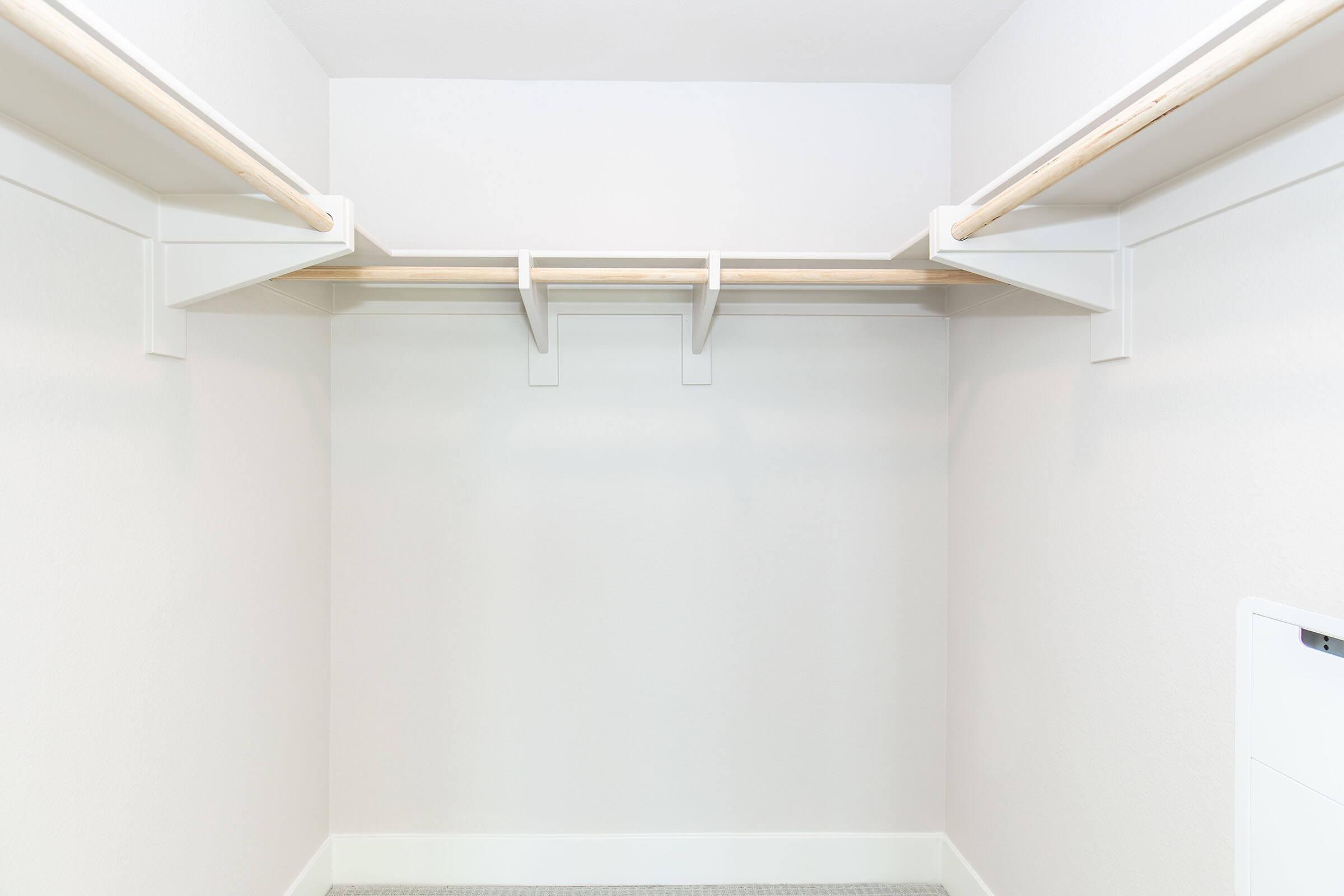 A clean and empty closet with two hanging rods on the sides and a single shelf above, all set against plain white walls. The floor is bare, creating a spacious and minimalist appearance.