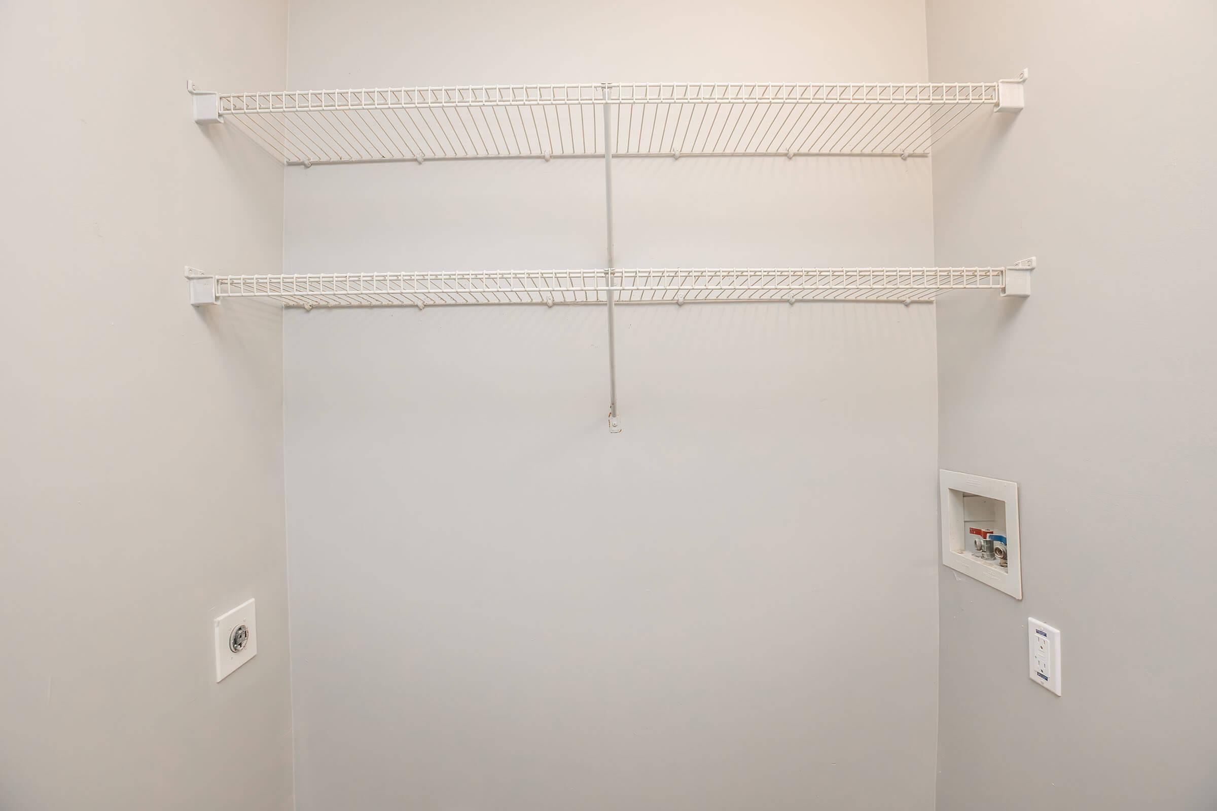 Empty closet space featuring two metal wire shelves on the wall. The walls are painted in a neutral color, and there is a small electrical panel and light switch on one side.