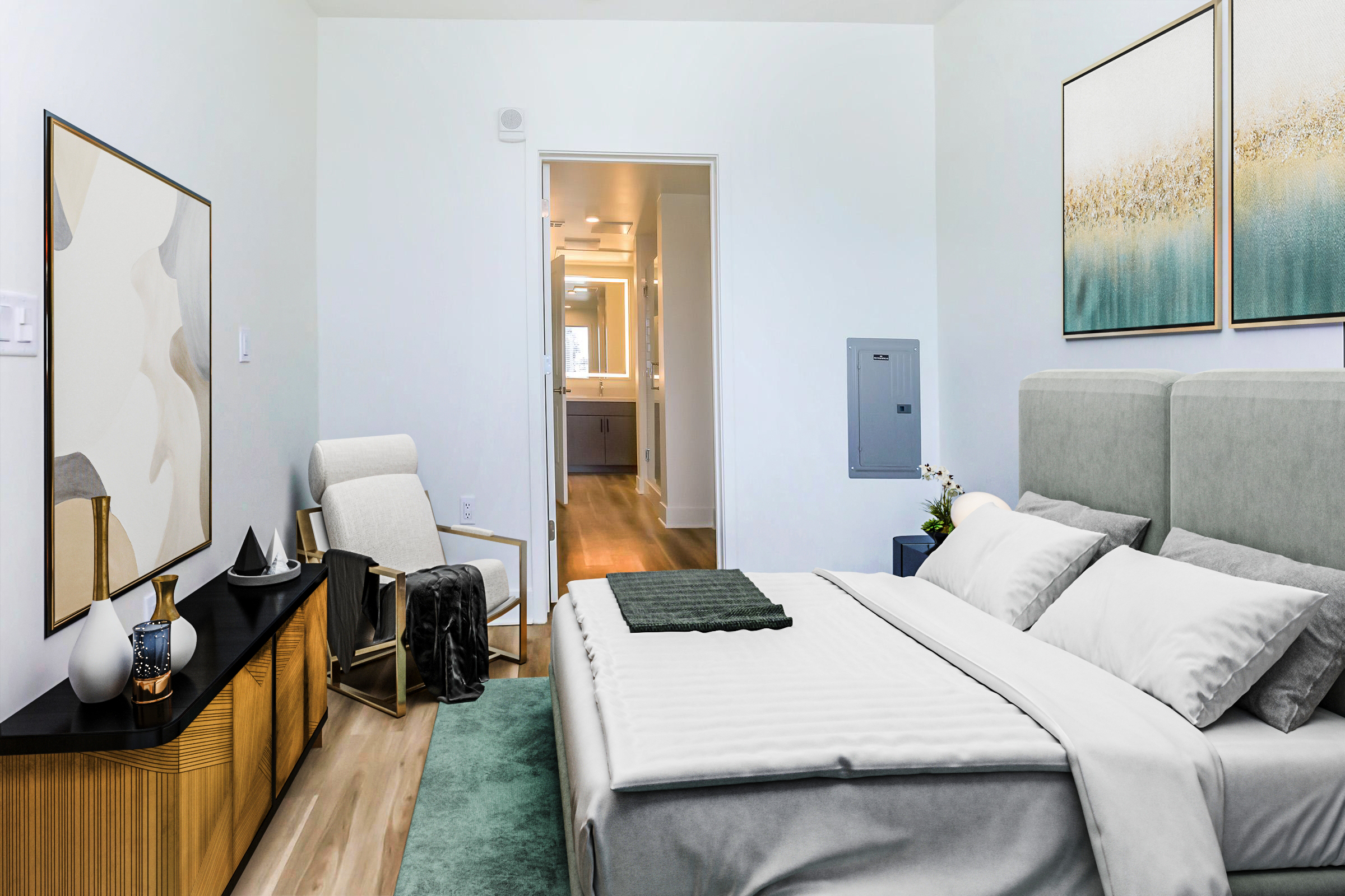 A modern bedroom featuring a light color palette. It has a comfortable bed with white linens and a gray throw, a cozy armchair in the corner, and a wooden dresser adorned with decorative items. Artwork is displayed on the wall, and a doorway leads to a bright bathroom, creating an airy atmosphere.
