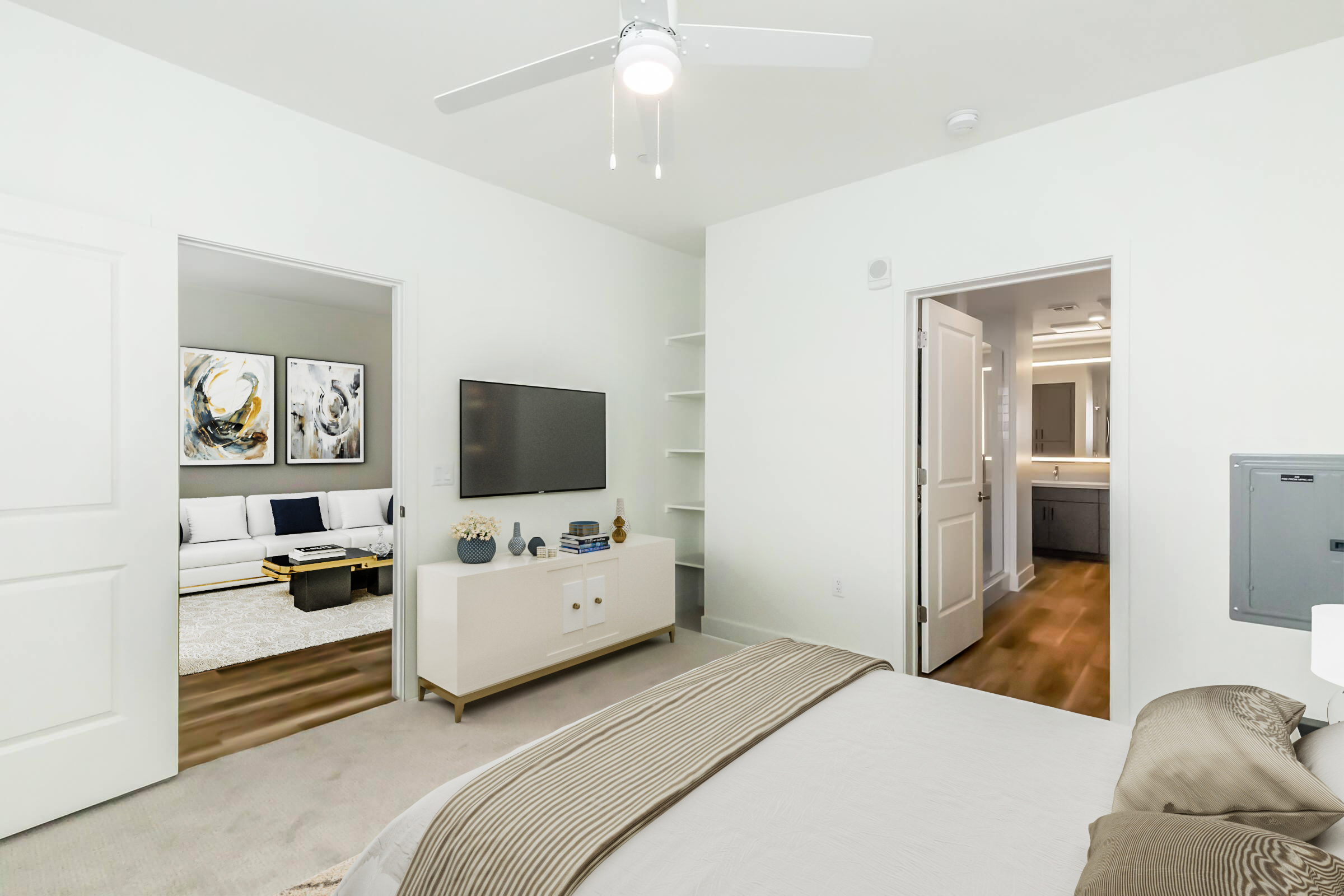 A bright, modern bedroom featuring a bed with decorative pillows, a dresser with a television, and a ceiling fan. Two doorways lead to a well-lit living area and a bathroom. The walls are painted white, and the flooring is light wood. Soft carpet covers the bedroom floor.