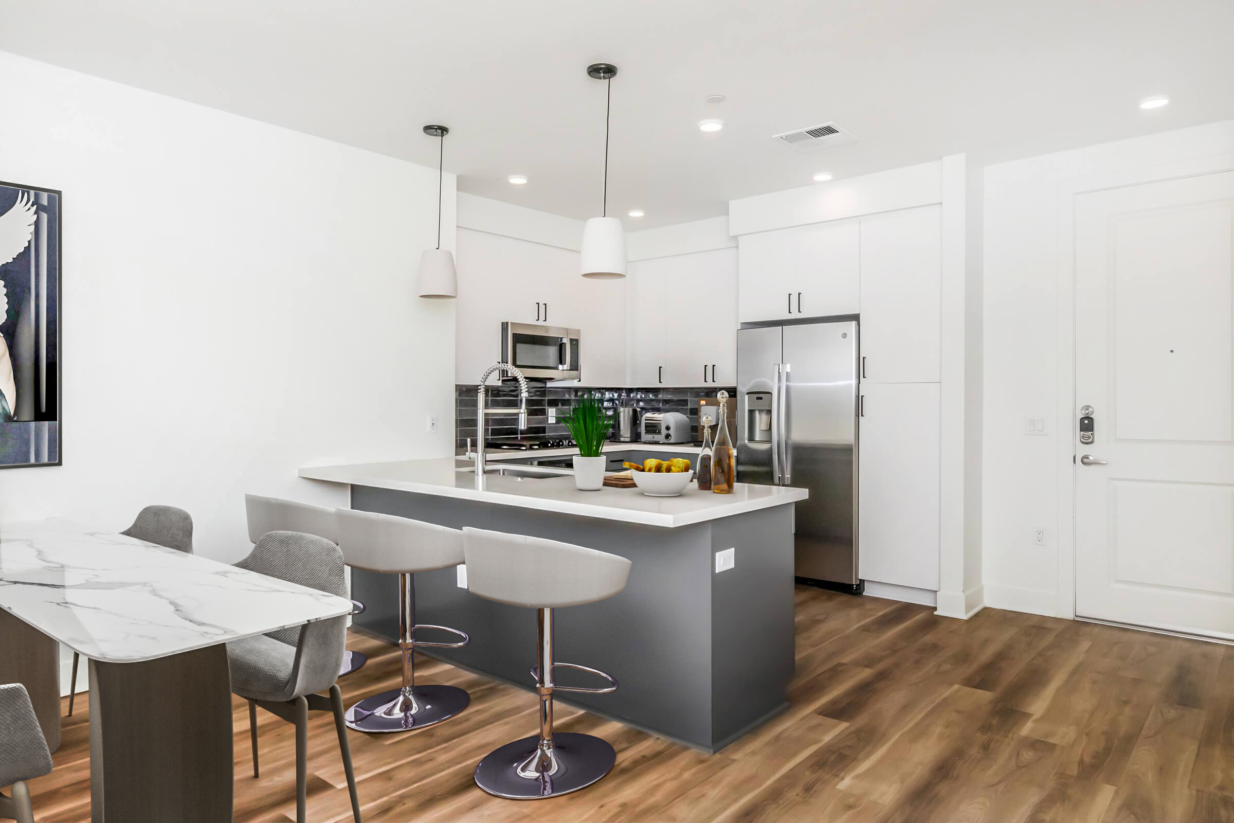Modern kitchen and dining area featuring a large island with bar seating, marble countertops, and sleek stainless steel appliances. The space is well-lit with recessed lighting, has white cabinets, and a wood floor that complements the contemporary design. A dining table is positioned nearby.