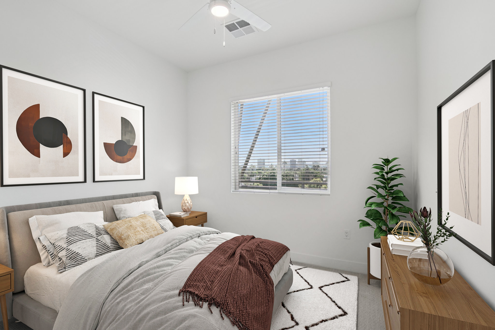 A modern bedroom featuring a cozy bed with decorative pillows and a textured blanket. Two framed abstract artworks hang above the bed. A sleek nightstand with a lamp is on one side, and a stylish dresser with a plant and decorative items is against the wall. A window provides natural light and a view outside.