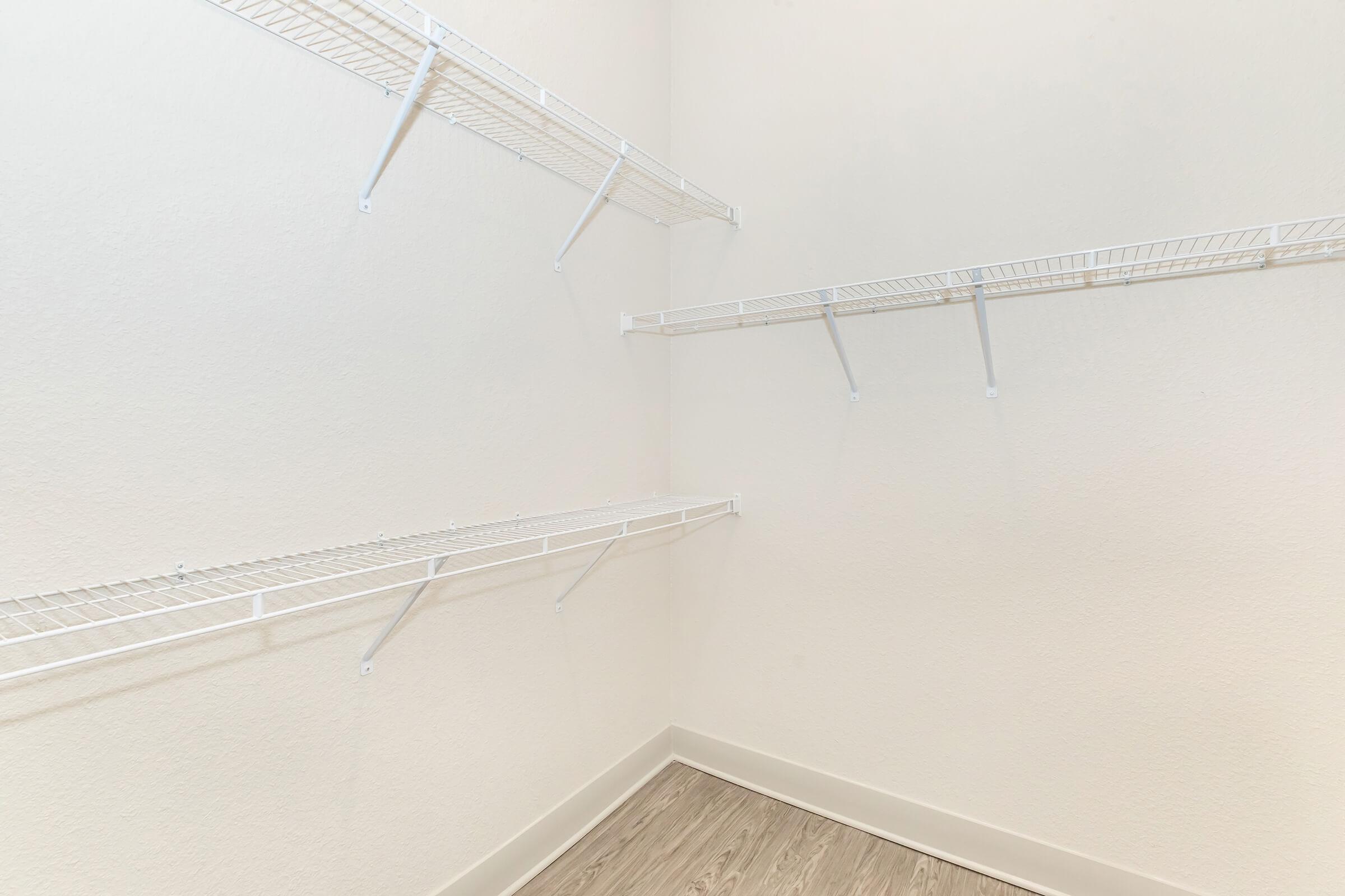 Empty storage room with white wire shelving mounted on the wall. The walls are painted a light, neutral color, and the floor has a light wood finish, creating a clean and spacious appearance.