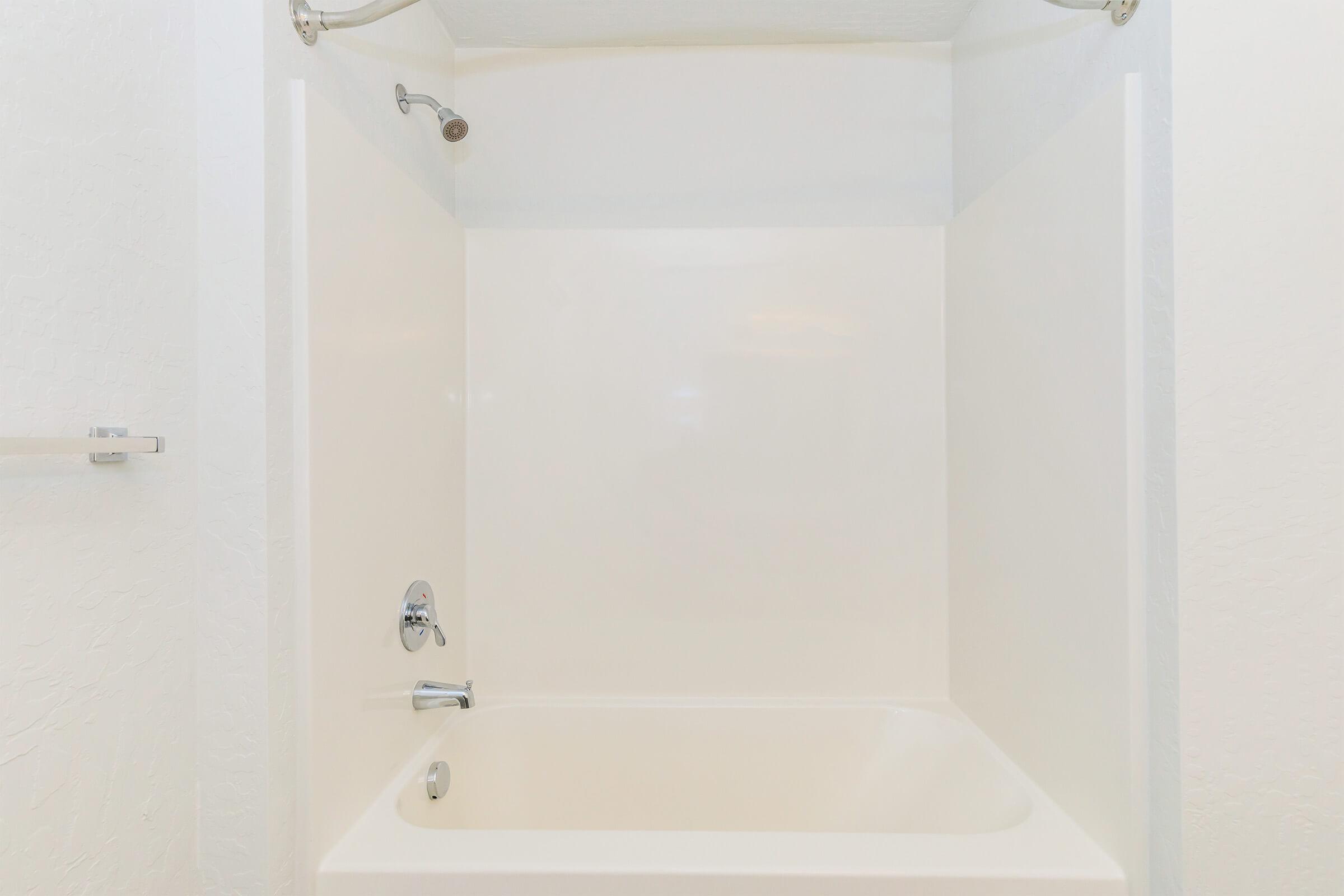 A clean, empty bathtub with a simple design, featuring a chrome faucet and showerhead. The surrounding walls are smooth and white, creating a minimalist look. Ideal for a bathroom setting, emphasizing cleanliness and simplicity.