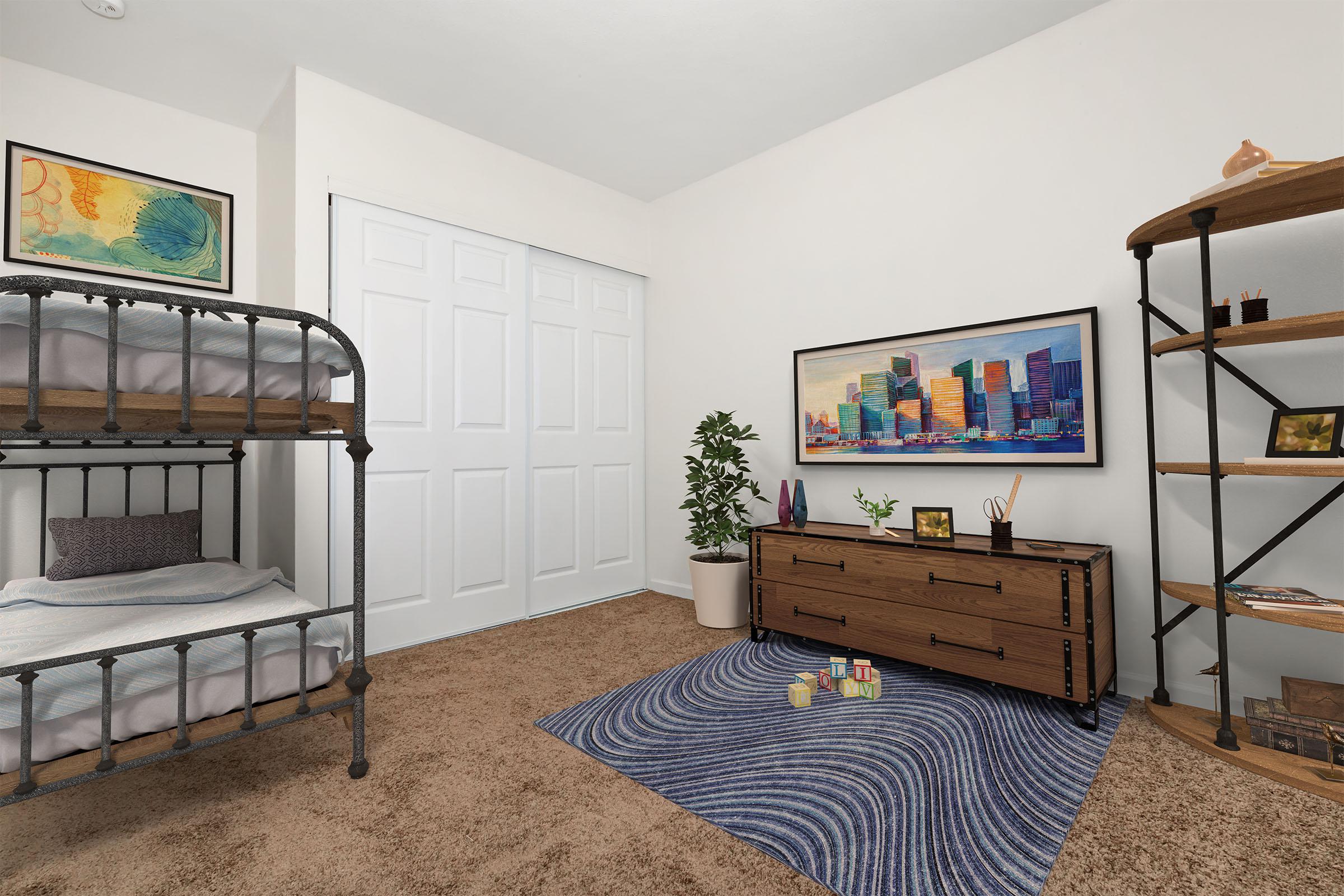 A cozy bedroom featuring a bunk bed with a simple white bedding, a wooden dresser, a patterned rug, a plant in a pot, and a bookshelf with decorative items. The walls are painted neutral, with a vibrant cityscape artwork and a colorful framed piece adding visual interest. A sliding door closet is visible in the background.