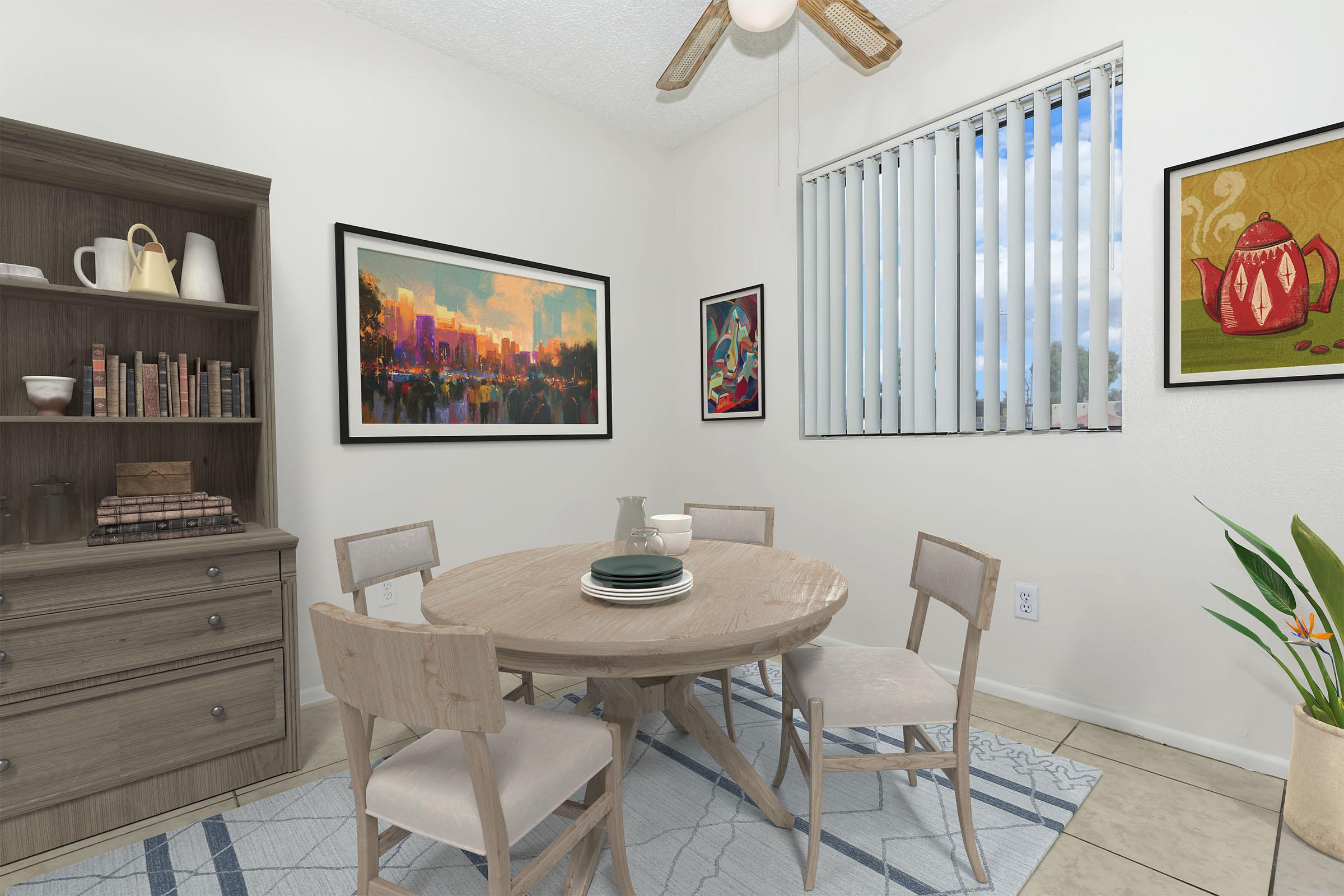 A cozy dining area featuring a round wooden table surrounded by four light-colored chairs. A bookshelf with books and decorative items is on one side, while colorful artwork adorns the walls. A large window with vertical blinds lets in natural light, and a potted plant adds a touch of greenery to the space.