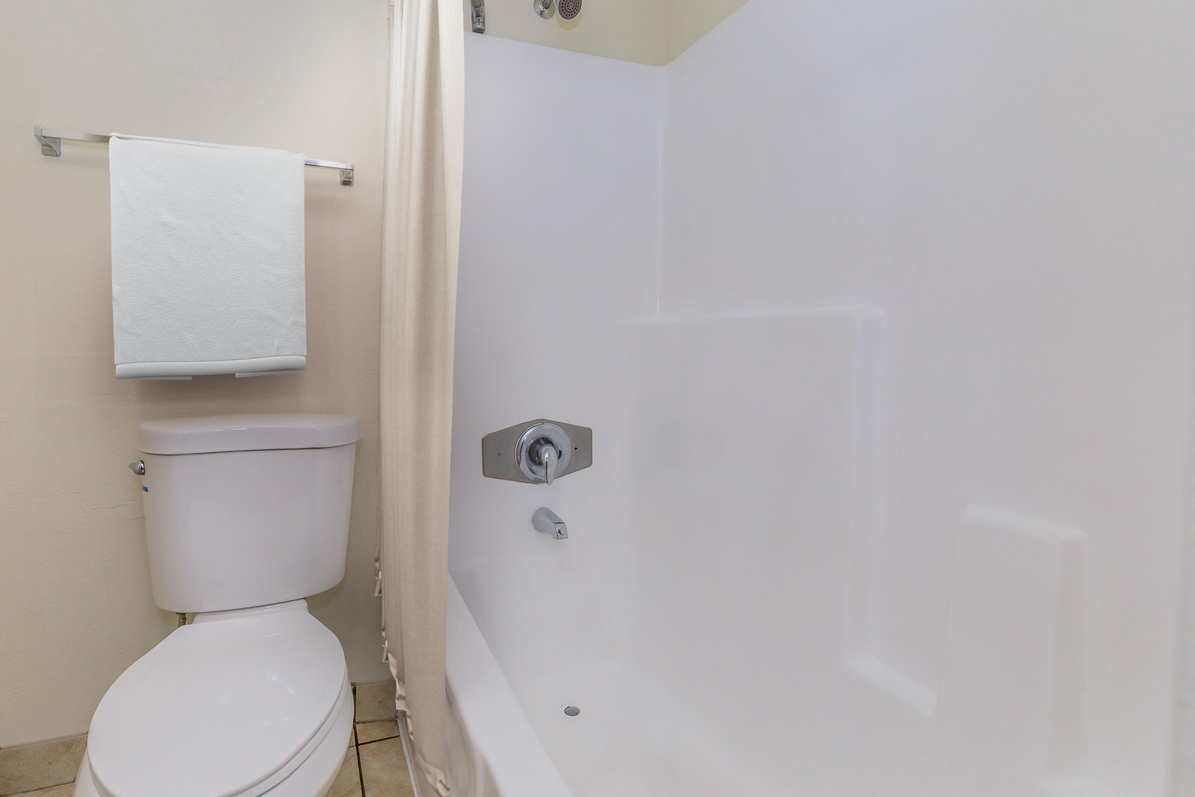 A clean and modern bathroom featuring a white bathtub, a toilet, and a shower curtain. A towel rack with a white towel is mounted on the wall. The overall appearance is simple and uncluttered, with neutral-colored walls and tiles.