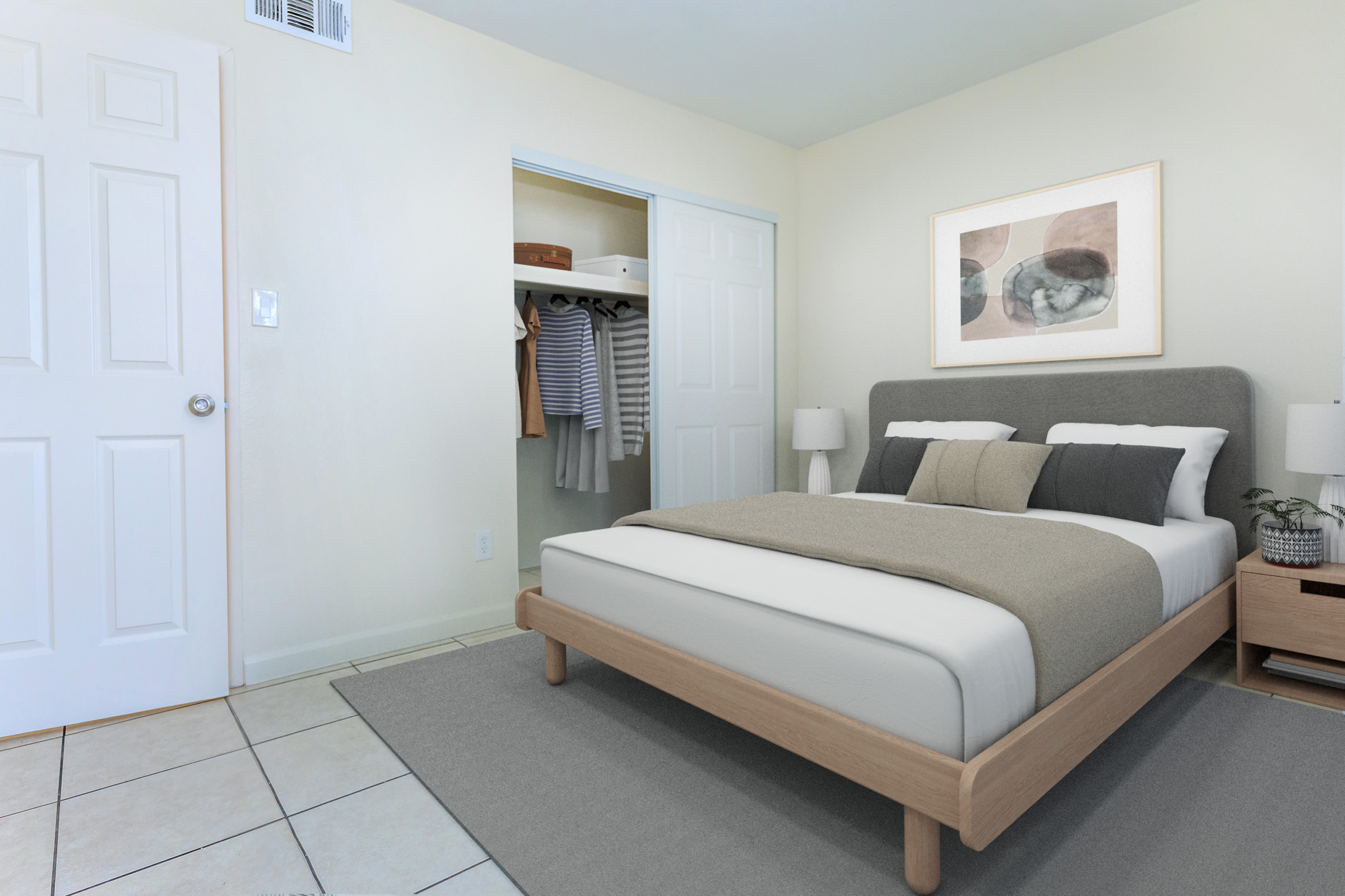 A cozy bedroom featuring a neatly made bed with gray and white bedding, flanked by two bedside lamps. A minimalistic art piece is hanging above the bed. To the side, a closet with partially open doors reveals hanging clothes. The room has light-colored walls and tiled flooring.