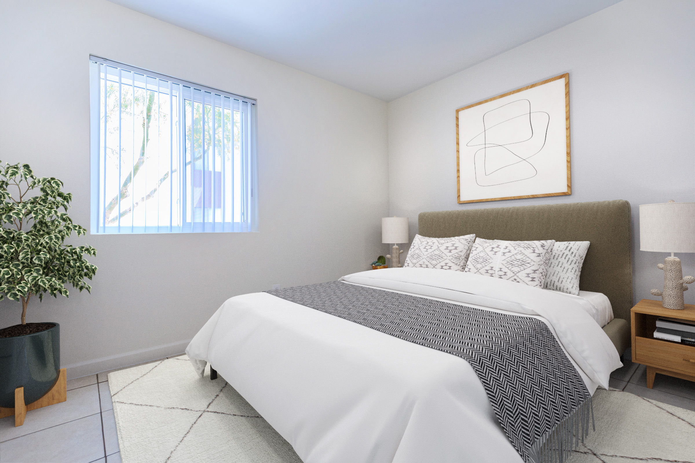 A cozy bedroom featuring a queen-sized bed with a gray and white patterned throw blanket. There are two decorative pillows on the bed, a wooden nightstand with a lamp, and a potted plant in the corner. Natural light filters through a window with blinds, illuminating the minimalist decor.