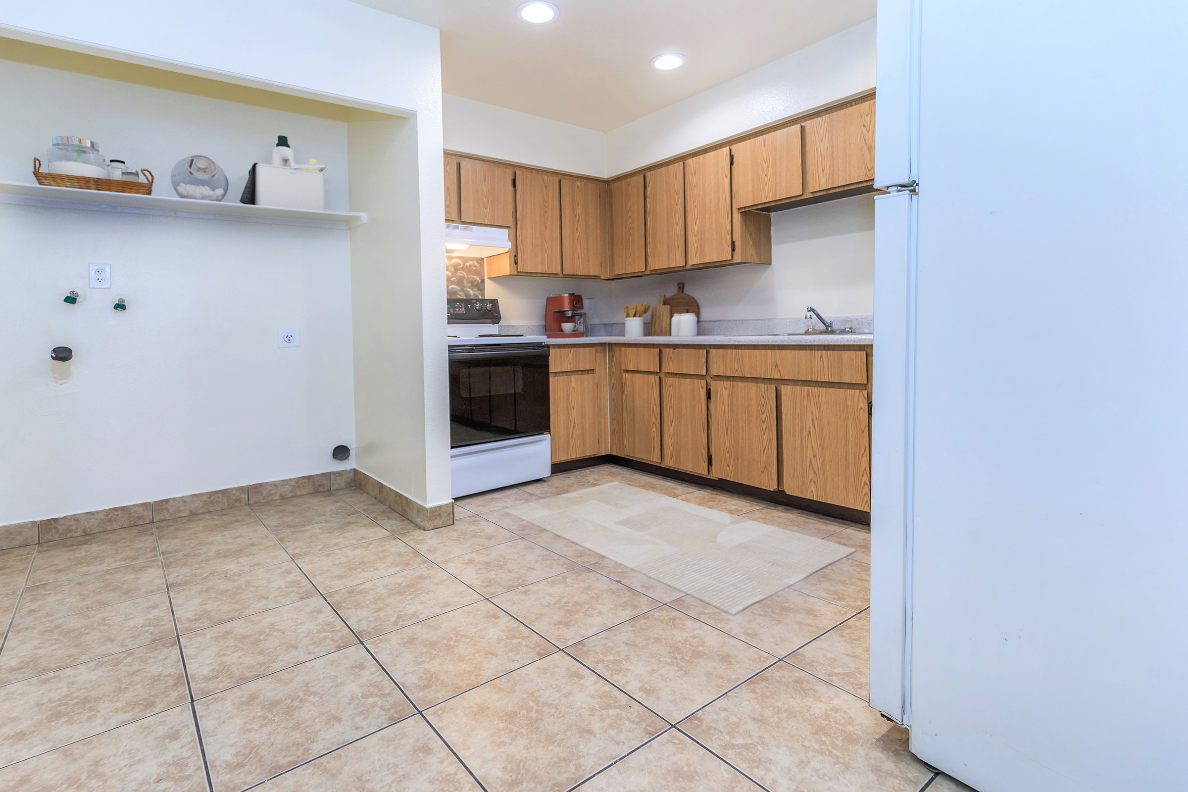 A clean, modern kitchen featuring wooden cabinets, a white countertop, and a built-in stove. The floor is tiled with light-colored tiles, and a small area rug is placed in the center. The walls are painted light colors, creating a bright and inviting atmosphere.