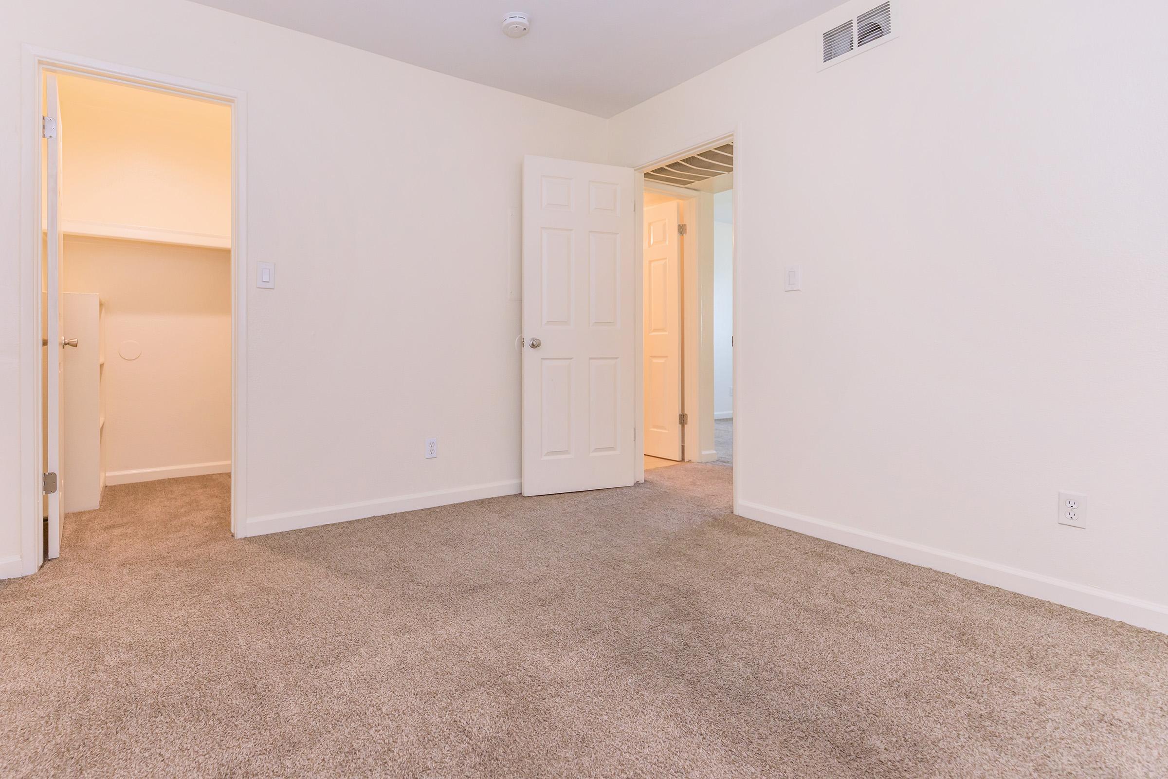 Empty room with beige carpet and light-colored walls. There are two doorways: one leading to what appears to be a closet and another to a bathroom. Natural light enters from the hallway, creating a bright and open atmosphere. The room is unfurnished and spacious, ideal for personal decoration.