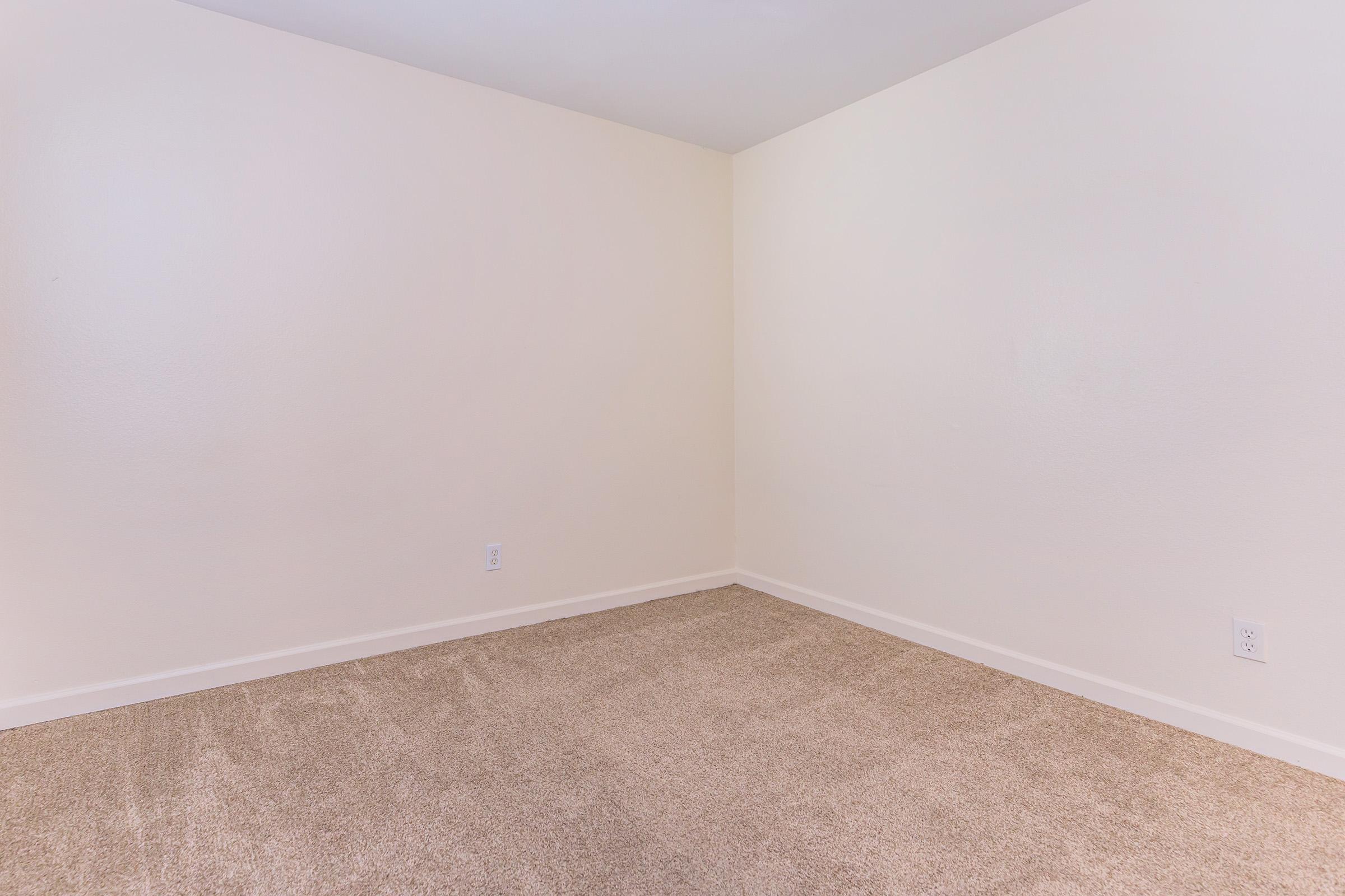 Empty room with beige walls and light brown carpet. There are no furnishings or decorations, creating a spacious and minimalist appearance. The lighting is soft, highlighting the neutral tones of the interior.