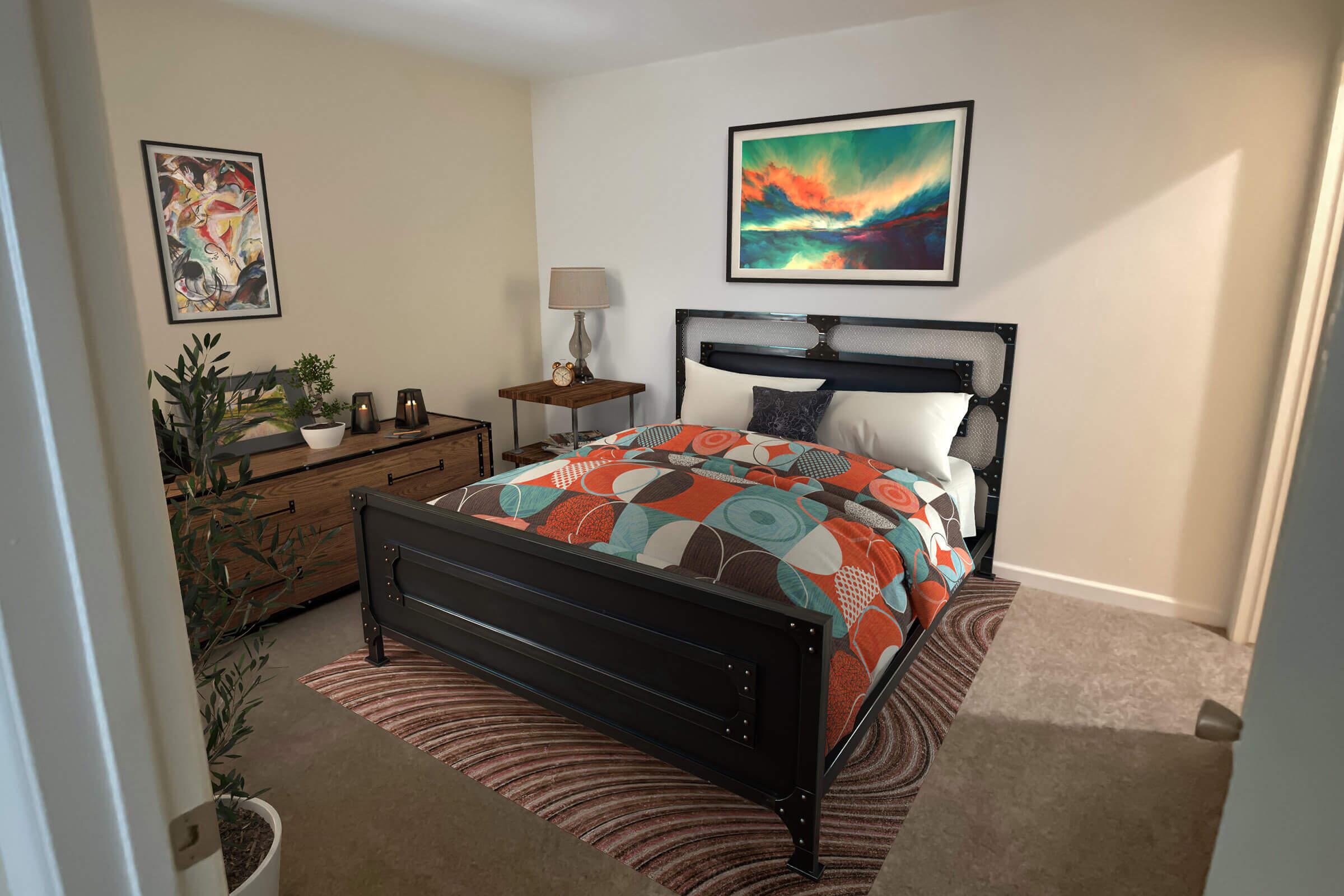 A cozy bedroom featuring a black metal bed with a colorful patterned comforter. There is a wooden nightstand with a lamp next to the bed and a dresser with decorative items. The walls are adorned with artwork, and a round rug adds warmth to the space. Soft sunlight streams in, creating a welcoming atmosphere.