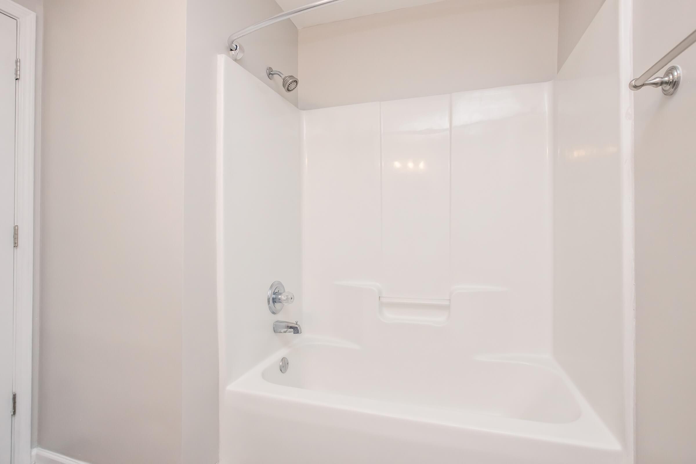 Clean and modern bathroom featuring a white bathtub with a shower curtain rod. The walls are painted in a light color, and there is a chrome faucet and showerhead. The space is well-lit, showcasing the simplicity and functionality of the design.