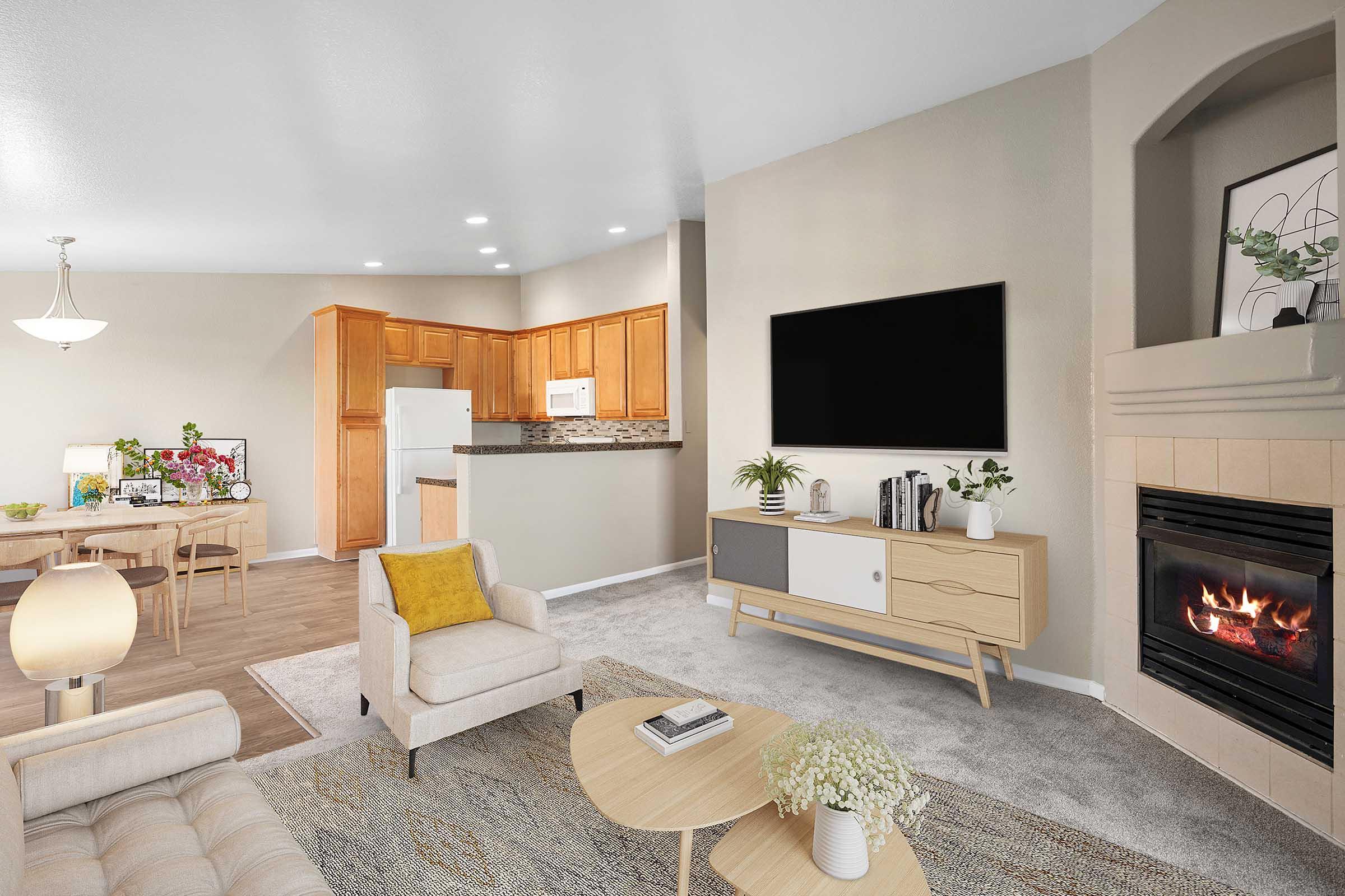 A cozy living room featuring a beige sofa and light wooden coffee table, with a decorative throw pillow. A modern TV unit with books and a plant stands to one side. The room has a gas fireplace, and an open kitchen area with wooden cabinets in the background. Soft lighting and neutral colors create an inviting atmosphere.