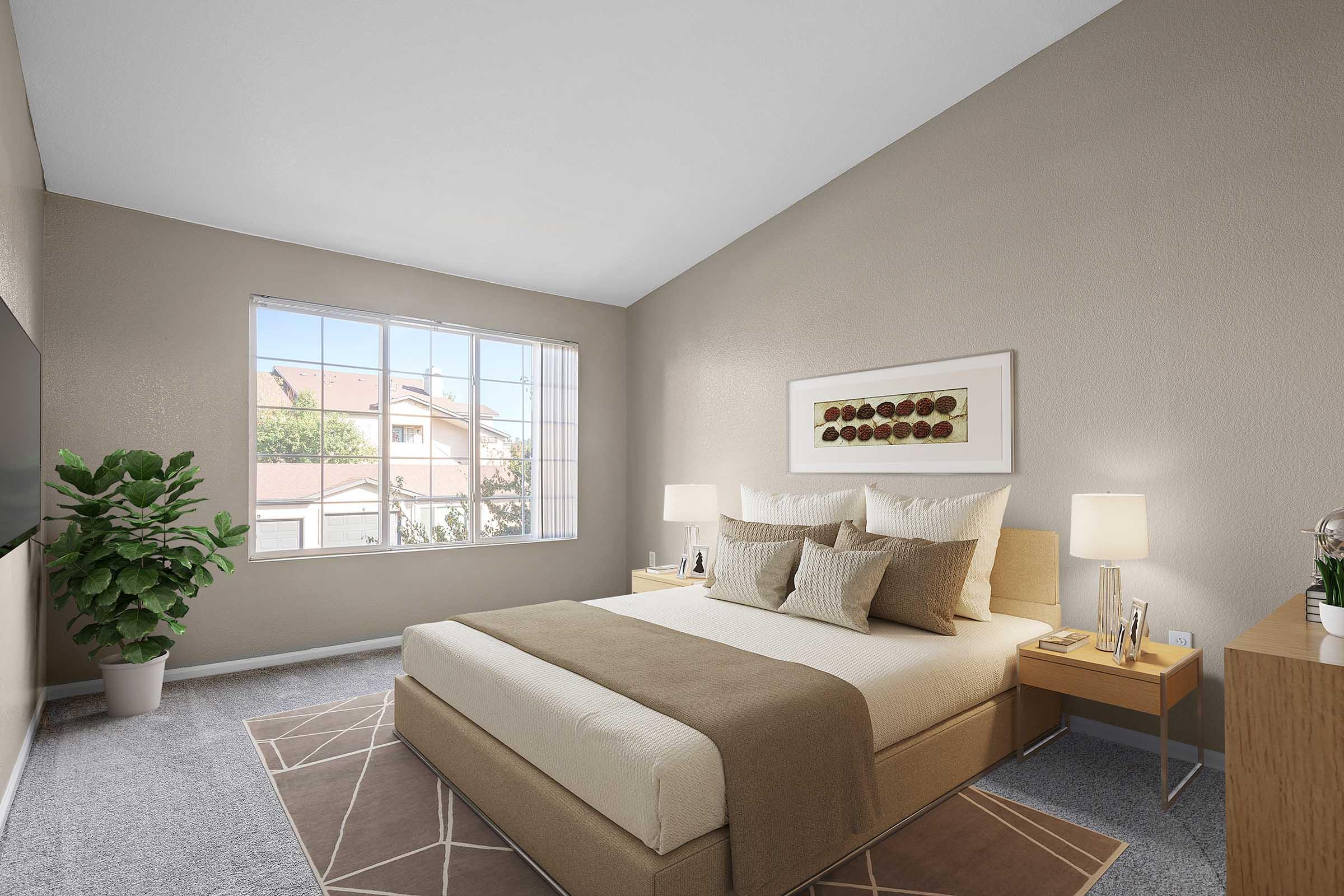 A well-decorated bedroom featuring a neutral color palette. It includes a large bed with beige and cream bedding, bedside tables with lamps, a modern artwork piece on the wall, and a potted plant in the corner. A large window lets in natural light, showing a view of residential buildings outside.