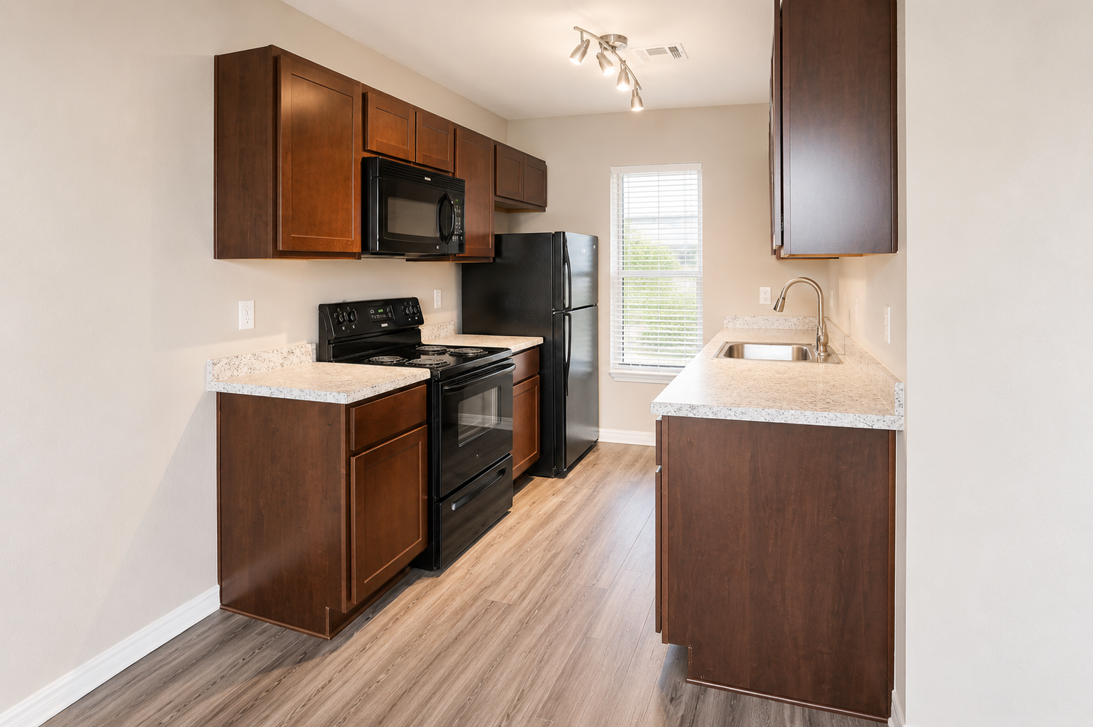 A modern kitchen featuring dark wood cabinets, black appliances including a stove, microwave, and refrigerator. The countertop is light-colored with a speckled design. A sink with a faucet is installed by the window, and the floor is covered with light wood-like laminate. Natural light streams in through the window.