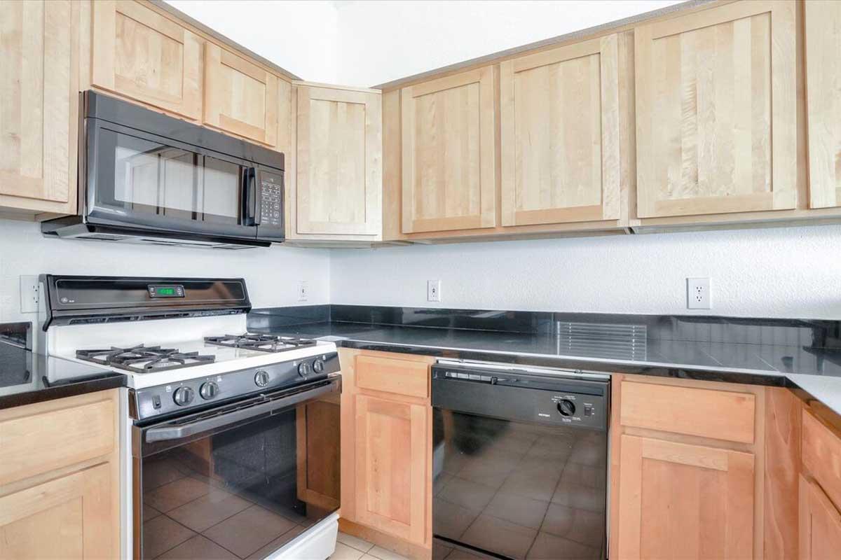 Modern kitchen featuring a black countertop, wooden cabinets, an electric stove with a microwave above, and a dishwasher. The design is clean and functional, with a bright and airy feel.