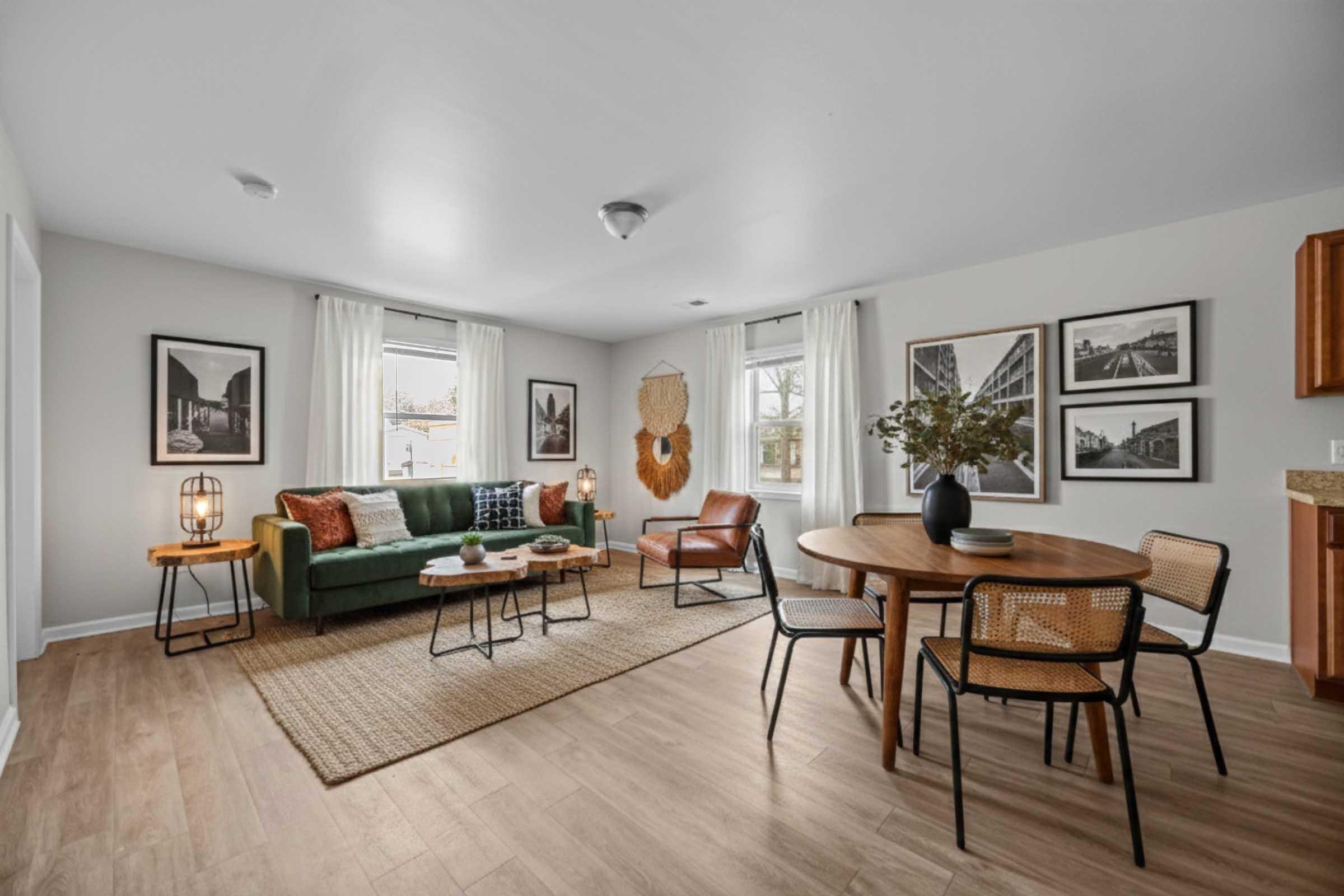 A bright and modern living space featuring a green sofa, a leather chair, and a wooden dining table with black chairs. The walls are adorned with framed photographs, and large windows let in natural light. A round area rug adds warmth to the floor, while decorative elements enhance the cozy atmosphere.