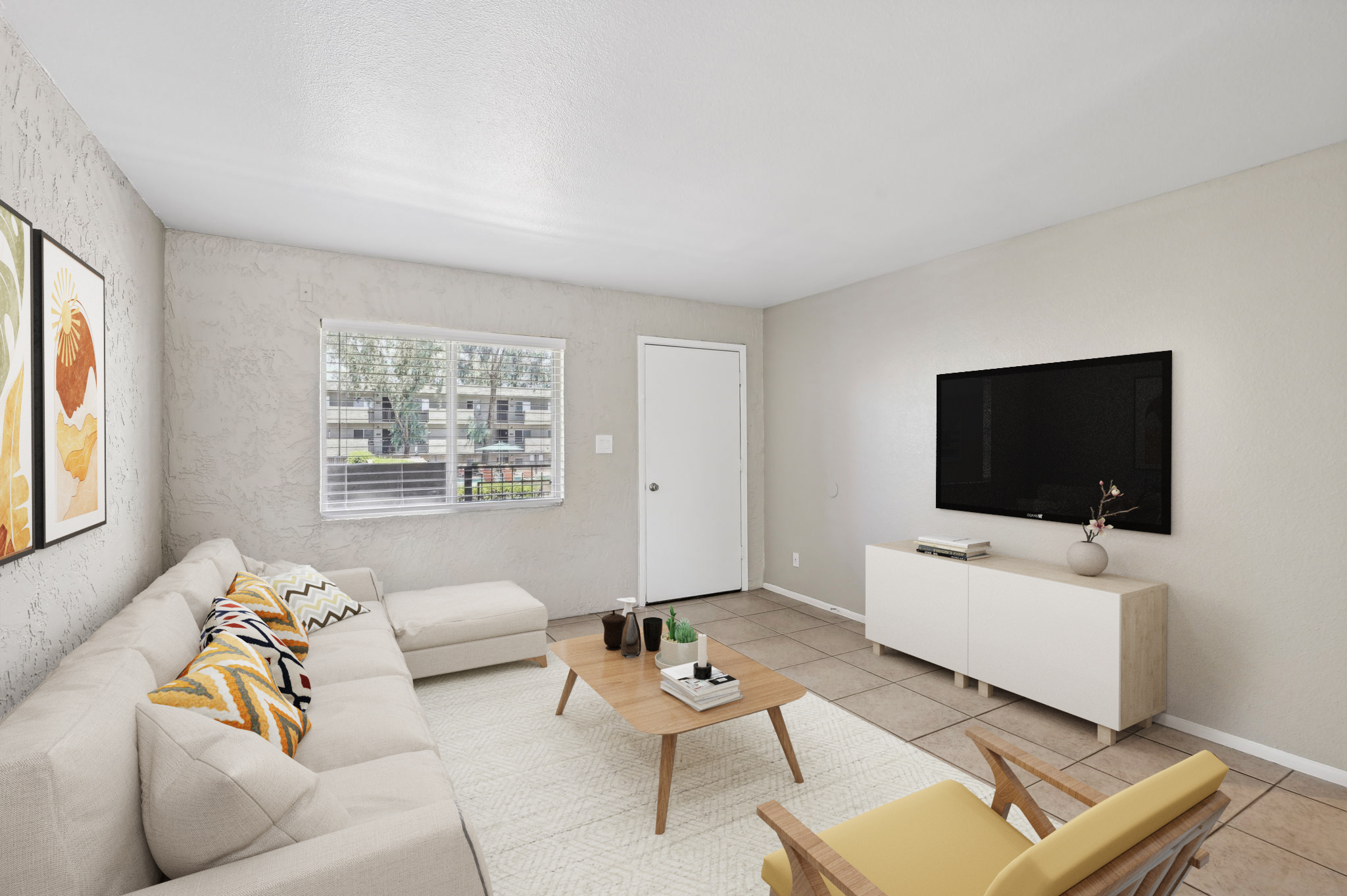 A modern living room featuring a beige sectional sofa with colorful cushions, a wooden coffee table, and a minimalist sideboard. A flat-screen TV is mounted on the wall, and there's a large window letting in natural light. Light-colored walls and tiled flooring complete the cozy ambiance.
