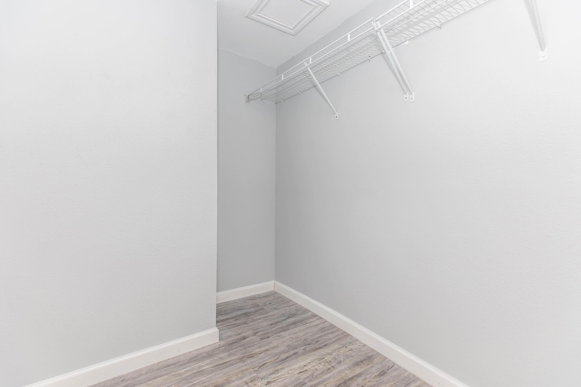 Empty walk-in closet featuring light grey walls, a wood-like laminate floor, and a wire shelving unit along one side. The space is bright and uncluttered, with no furnishings or items inside.