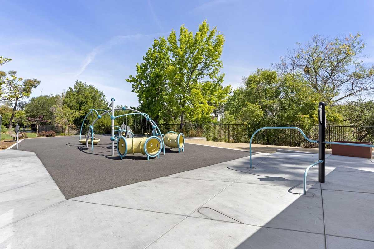 A playground featuring a modern climbing structure with blue and yellow elements on a rubberized surface.