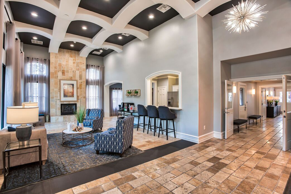 Modern living room with stylish furniture, arched ceilings, and large windows. A seating area features a circular coffee table and decorative plants, while a bar with high stools is visible in the background. The space has a warm color palette with a contemporary light fixture adding a touch of elegance.