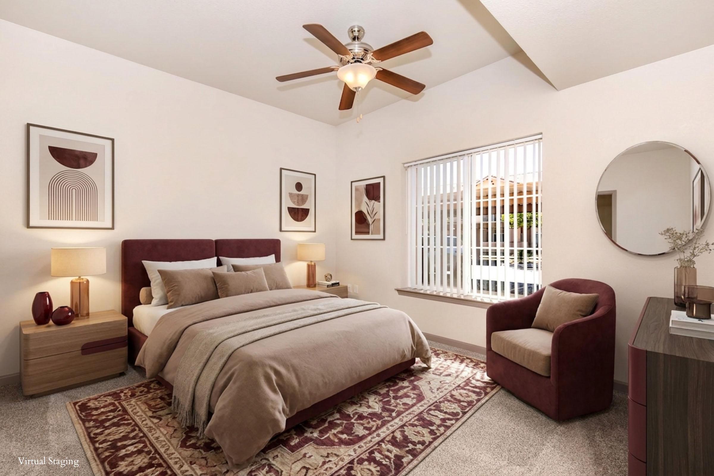 A cozy bedroom featuring a queen-sized bed with beige and brown bedding, two bedside lamps, a large window with white blinds, and a round mirror. The decor includes framed abstract art on the walls, a burgundy armchair, and a patterned area rug, creating a warm and inviting atmosphere.