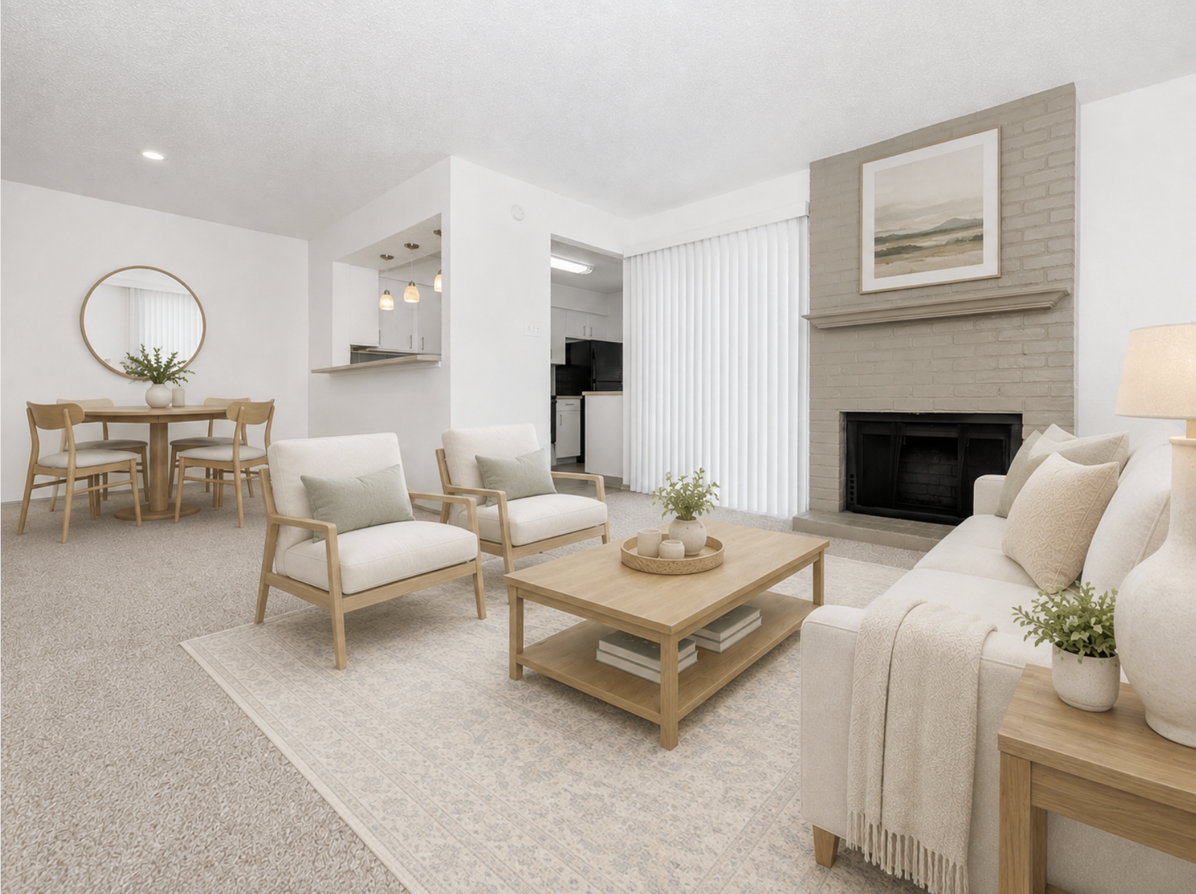 A modern living room featuring a light-colored sofa and armchairs, a wooden coffee table, and a cozy area rug. A fireplace is located on the right, with a wall-mounted artwork above it. In the background, there's a dining area with a round table and four chairs, and a kitchen visible through an open layout.