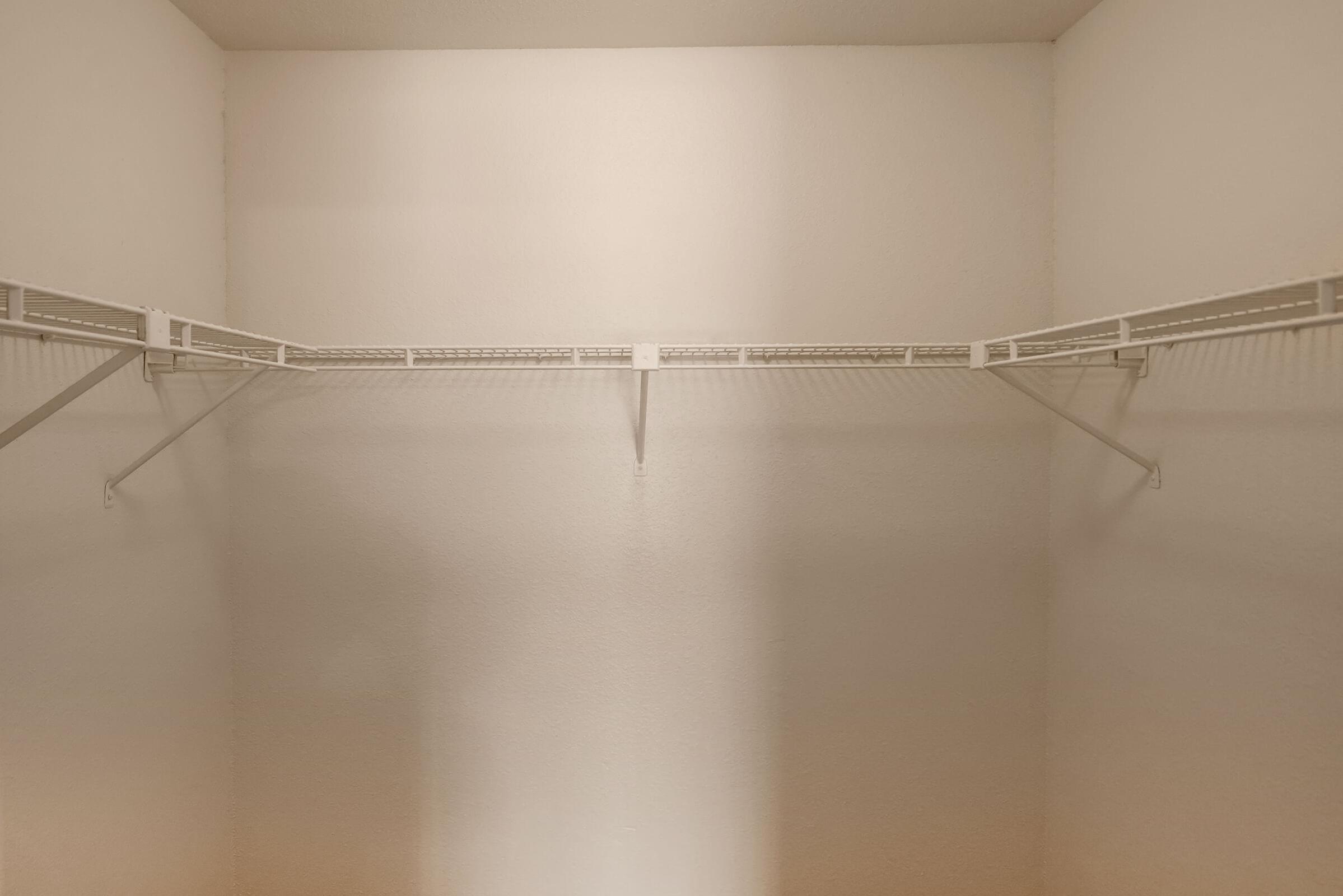 A minimalist closet interior featuring a bare wall with two white shelving units mounted along the sides, creating an open and spacious appearance. The lighting highlights the emptiness, suggesting a lack of stored items.