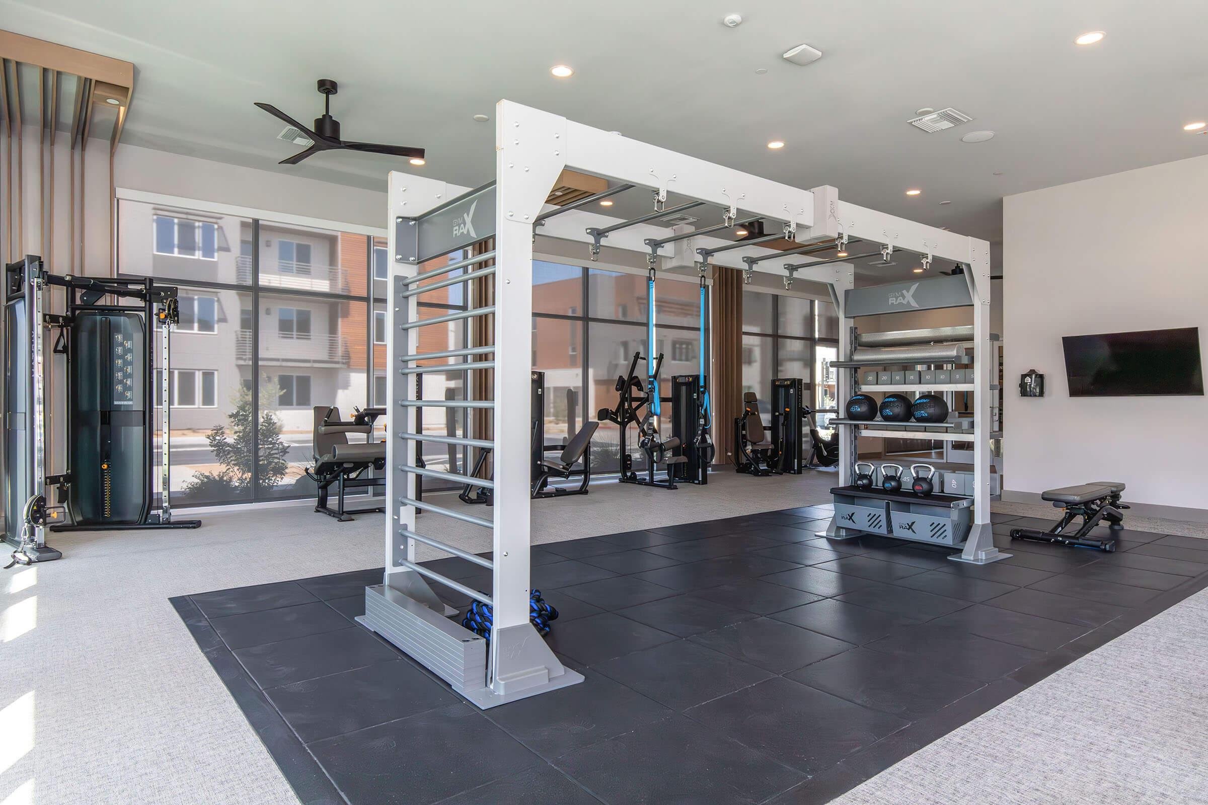 Modern gym interior featuring a multi-use strength training rig, surrounded by various fitness equipment including weights and benches. The space is well-lit with large windows, showcasing a clean and inviting atmosphere for workouts.