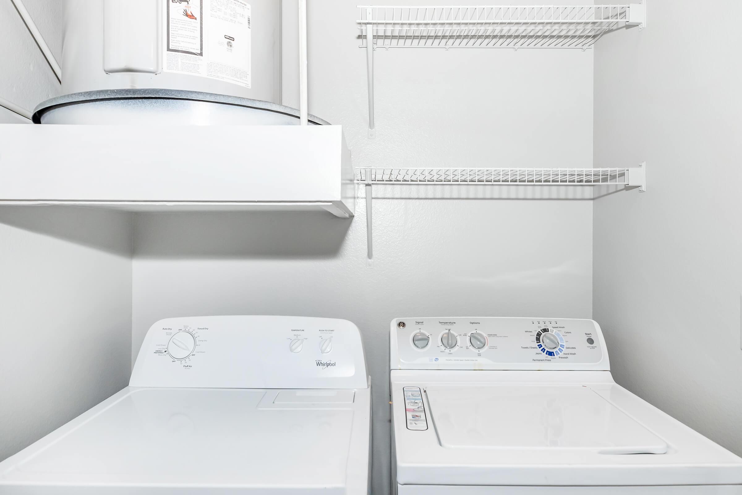 A clean and organized laundry room featuring a white washing machine and dryer. Above the appliances is a shelf with a water heater, and there are wire shelves on the wall for additional storage. The walls are painted a light color, giving the space a bright and airy feel.