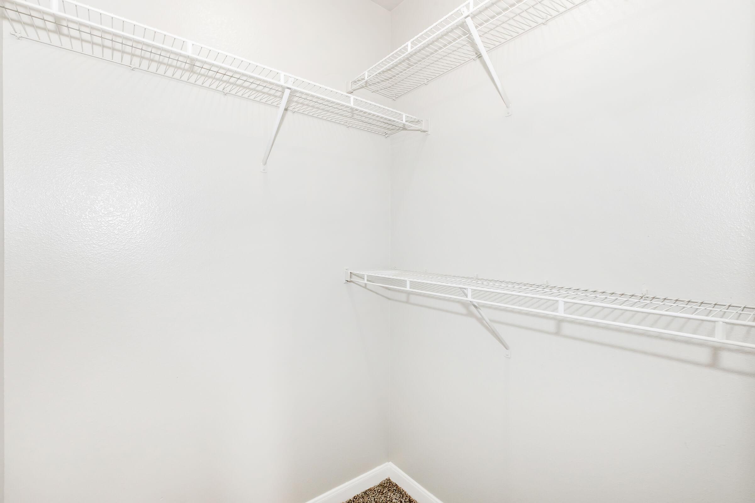 Empty walk-in closet with white walls and wire shelving on two sides. The floor has a pebbled texture, and there are no items stored on the shelves. The overall space appears bright and clean, emphasizing simplicity and minimalism.
