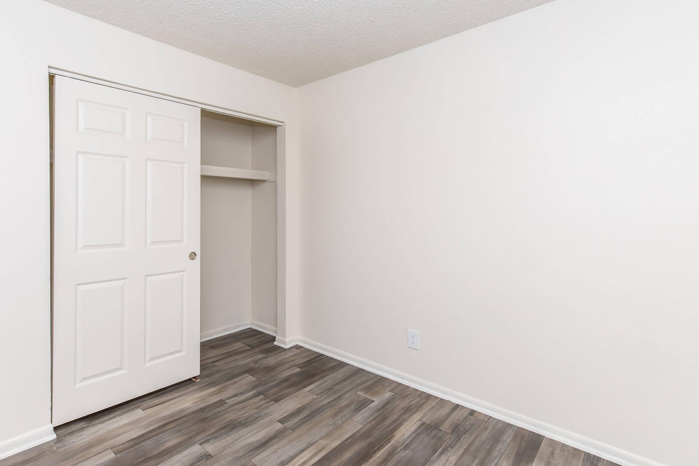 Empty room with light-colored walls and a wooden floor. There is a closet with double doors on the left side, and the room has no furniture. The overall atmosphere is clean and minimalistic.