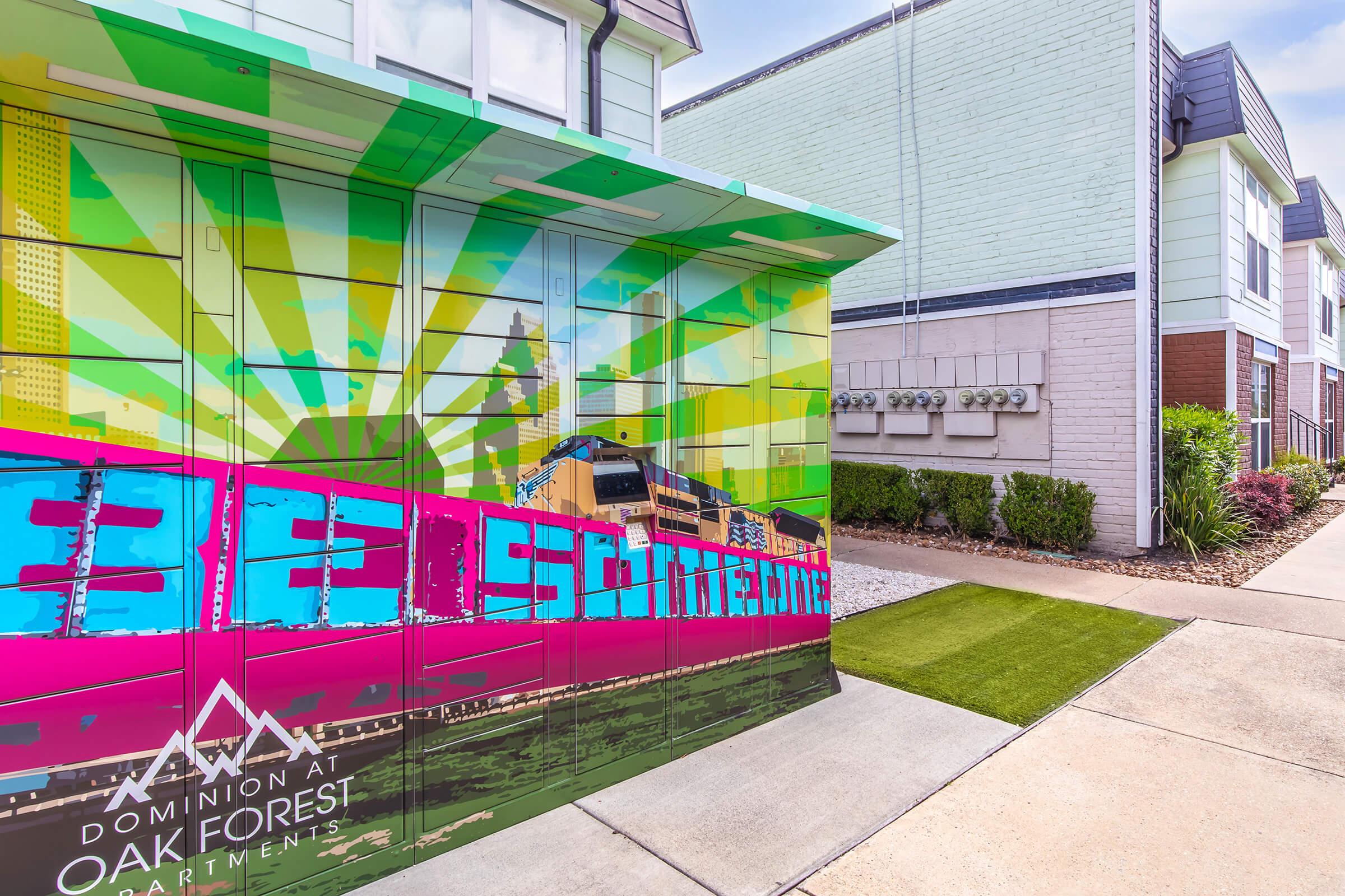 Colorful and modern outdoor mailboxes at the Dominion at Oak Forest Apartments, featuring vibrant graphics and a sunny, cheerful design. The backdrop includes a well-maintained walkway and adjacent buildings, enhancing the inviting atmosphere of the apartment complex.