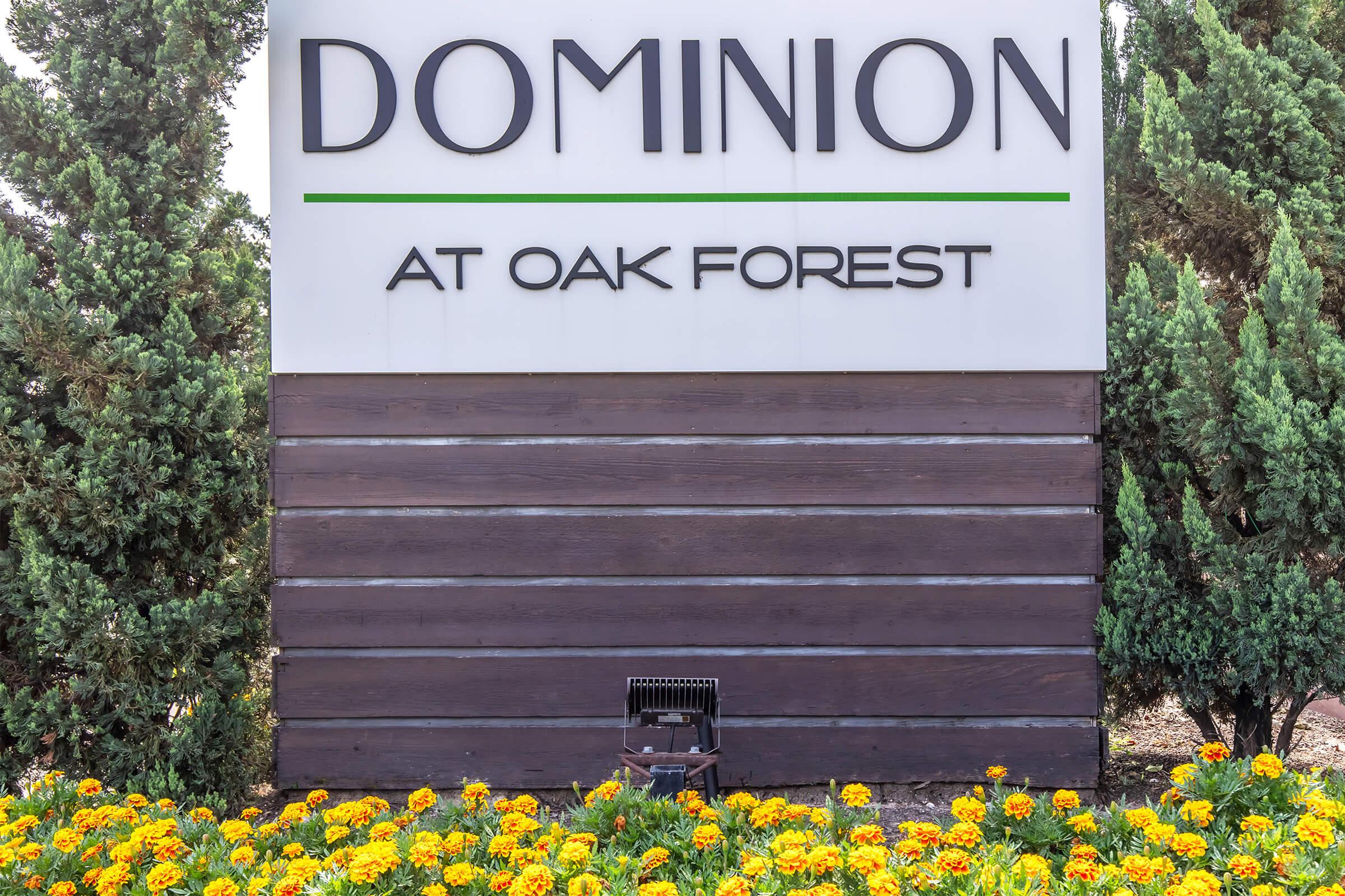 Sign for "Dominion at Oak Forest" surrounded by greenery and vibrant yellow flowers in a landscaped area.