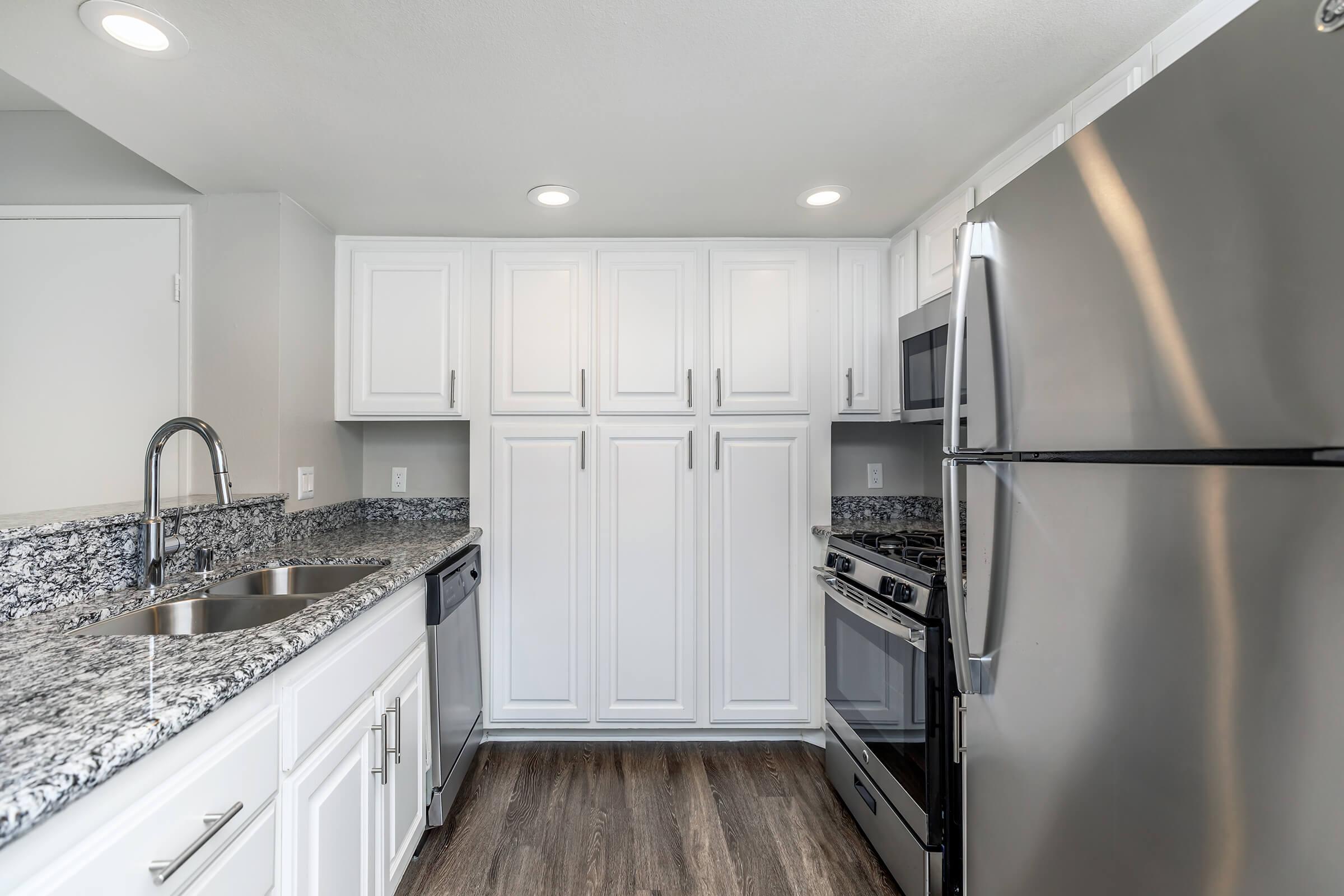 Modern kitchen featuring white cabinetry, stainless steel appliances including a refrigerator and oven, and a granite countertop with a double sink. The space has recessed lighting and a warm, inviting layout, showcasing a clean and contemporary design.