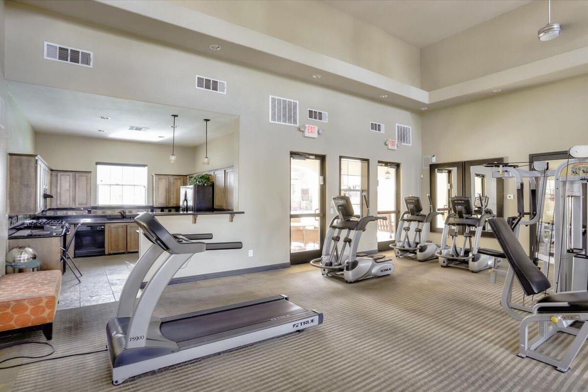 A modern gym interior featuring several treadmills, weights machines, and a sleek design. The space is well-lit with large windows and neutral-colored walls. There is a workout area with fitness equipment and a small counter area in the background, creating a welcoming atmosphere for exercise.