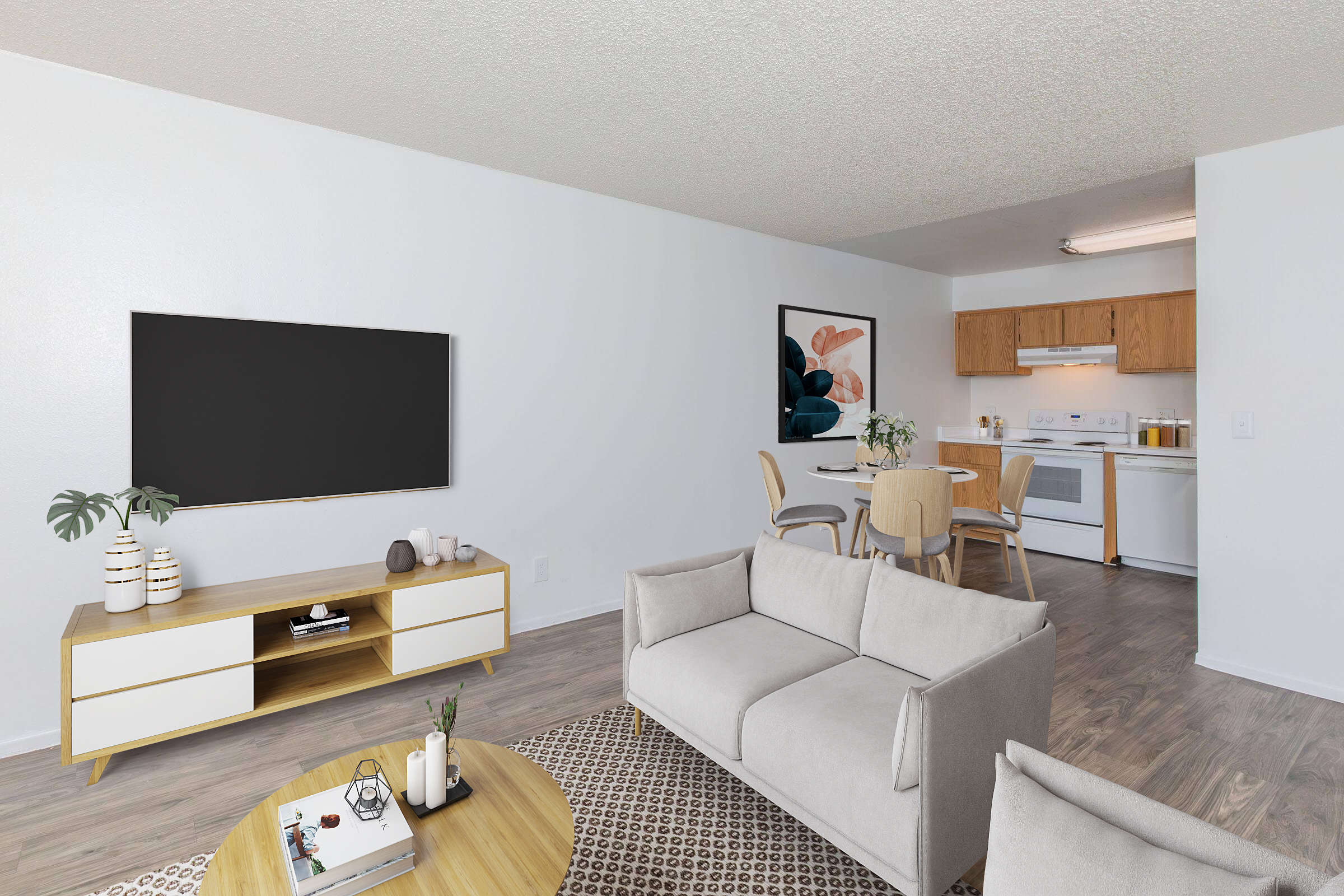 A modern living room and dining area featuring a light gray sofa, wooden coffee table, and a large flat-screen TV mounted on the wall. There's a round area rug, decorative plants, and a light-colored dining table with chairs adjacent to a kitchen equipped with white appliances and wooden cabinets.
