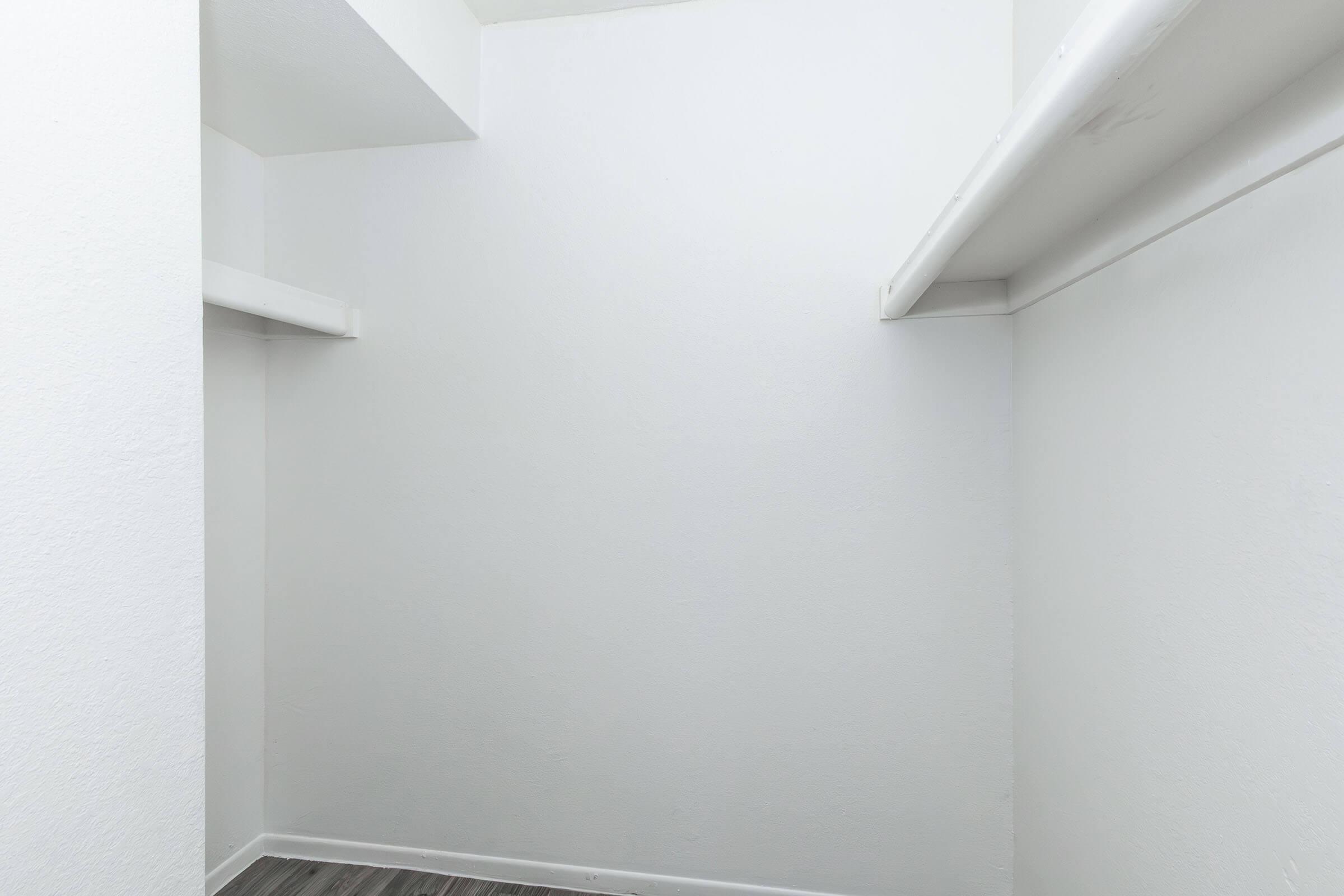 A clean, empty closet with white walls and two shelves. The floor is a light-colored laminate, and the overall space appears bright and uncluttered, suitable for storage or organization.