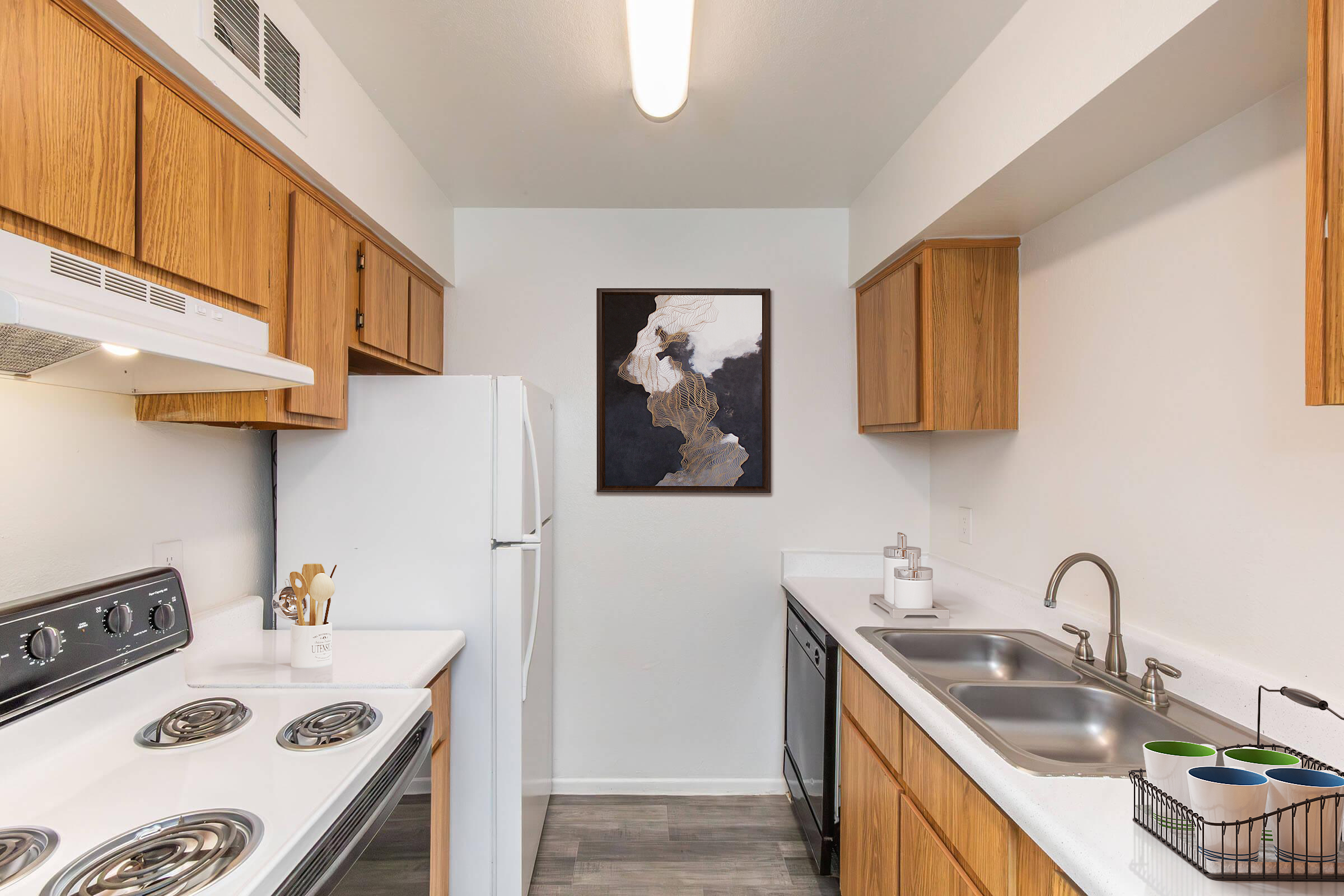 A modern kitchen featuring light-colored cabinetry, stainless steel appliances, a white countertop, and wood accents. The space includes a framed abstract artwork on the wall, a double sink, and an organized utensil holder, creating a clean and inviting atmosphere.
