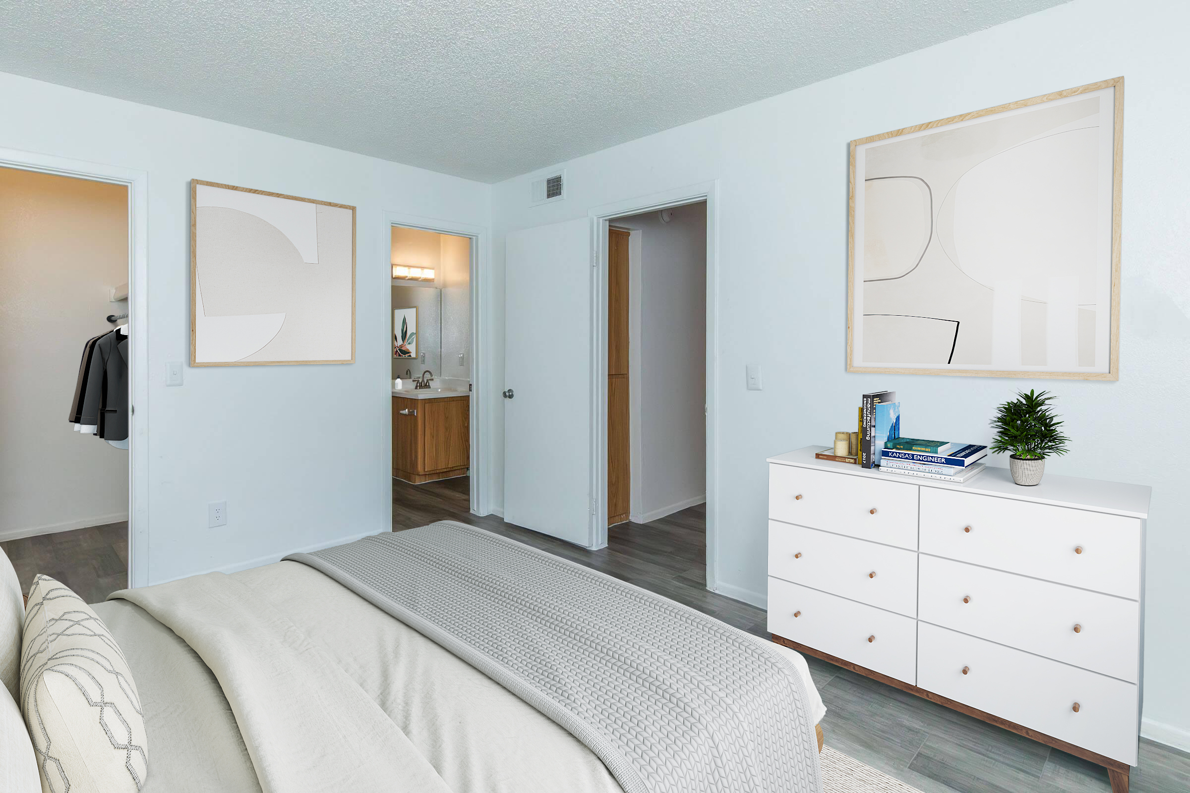 Bright bedroom featuring a neutral color palette, with a neatly made bed and decorative pillows. A white dresser sits against one wall, adorned with books and a small plant. Doorways lead to a closet and bathroom, adding functionality to the space. Modern artwork hangs on the walls, enhancing the minimalist aesthetic.
