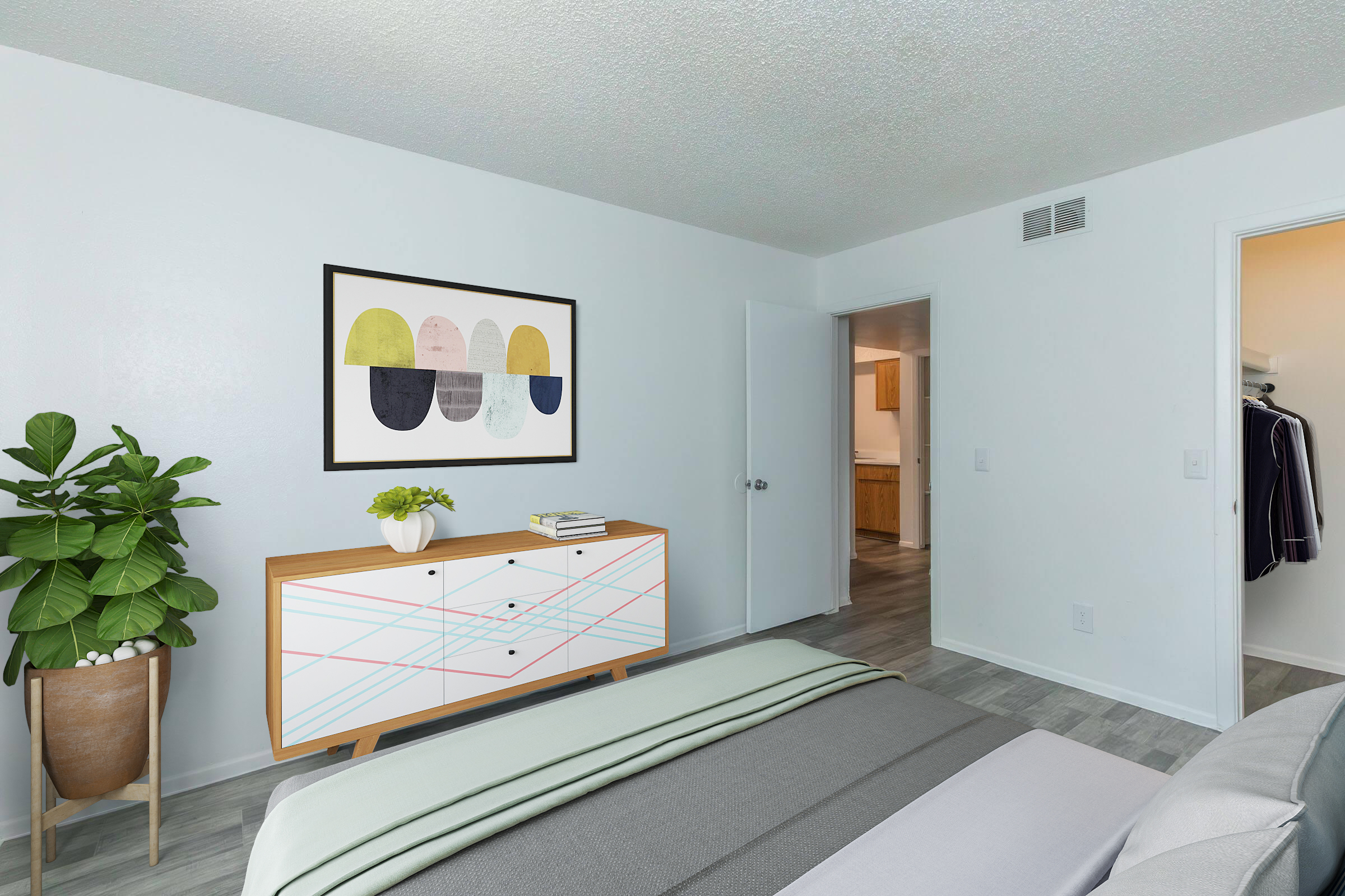 A bright and modern bedroom featuring a bed with soft linens, a decorative plant, and a stylish sideboard displaying artwork. The walls are painted white, and there’s a door leading to a kitchen area in the background, enhancing the open, airy feel of the space.