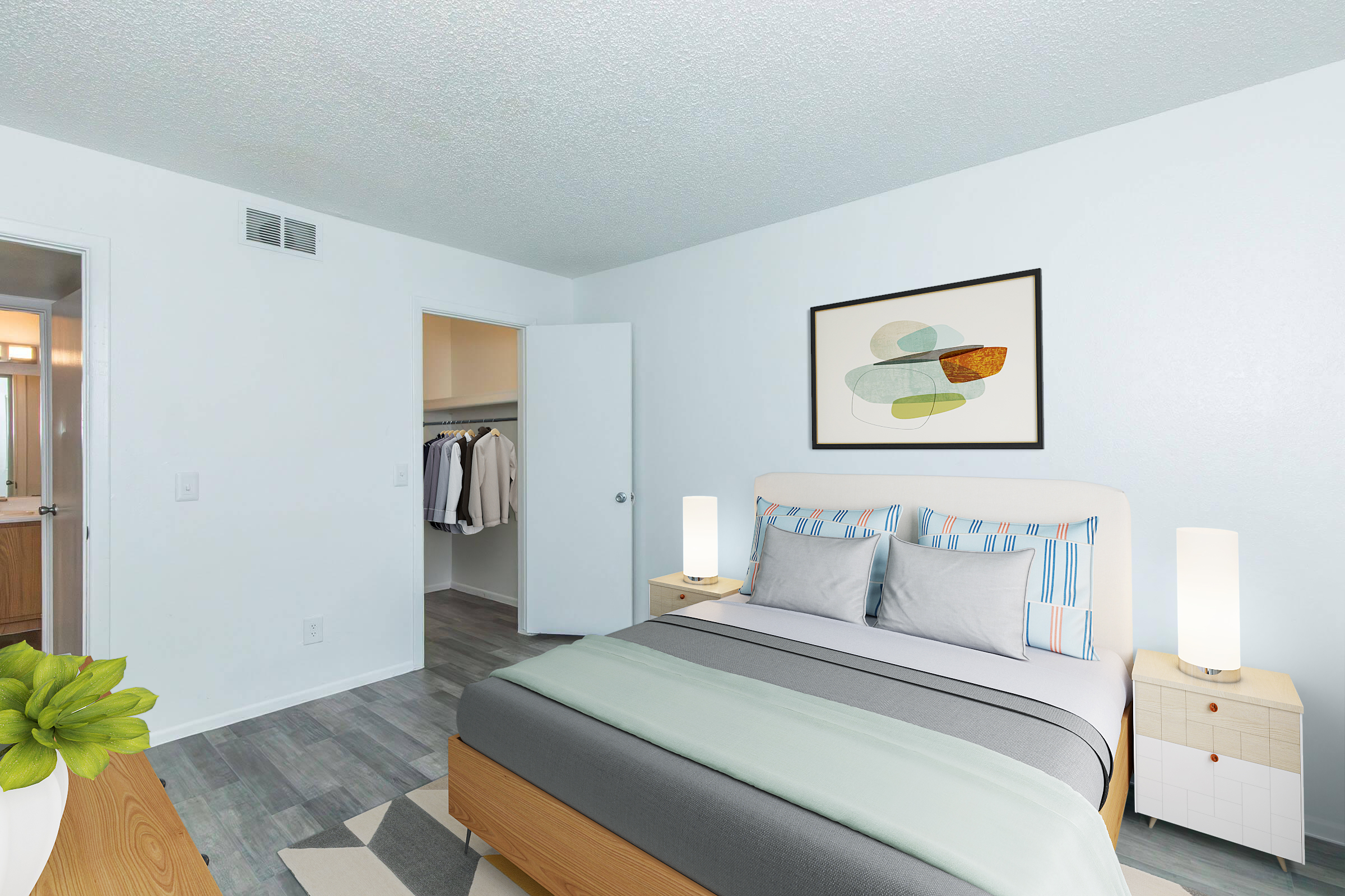 A bright and modern bedroom featuring a bed with light-colored bedding and decorative pillows. Two bedside lamps illuminate the space. A piece of abstract art hangs above the bed, and there's an open closet with clothes visible. The room has light blue walls and a cozy, welcoming atmosphere.