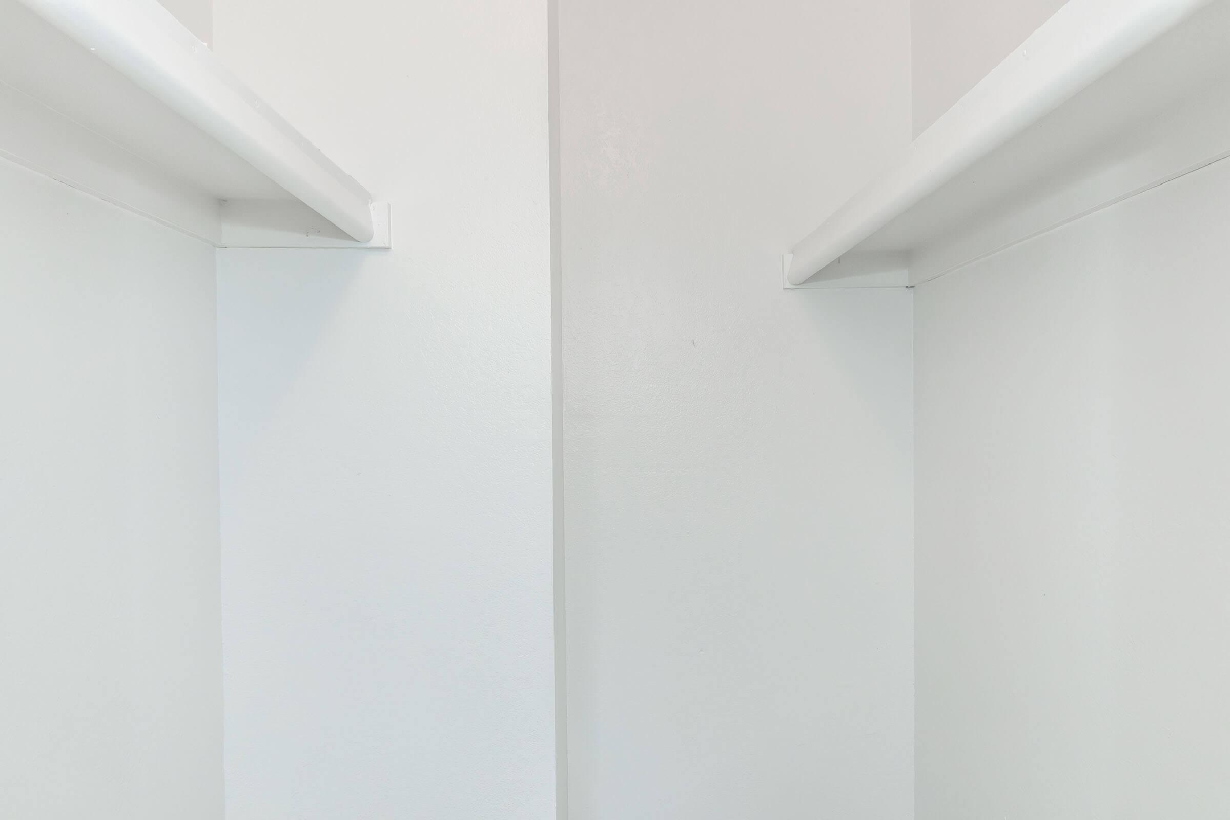 Empty white closet with two horizontal shelves on opposite sides and a clean, minimalistic design. The walls are smooth and devoid of any items, creating a spacious and organized appearance.